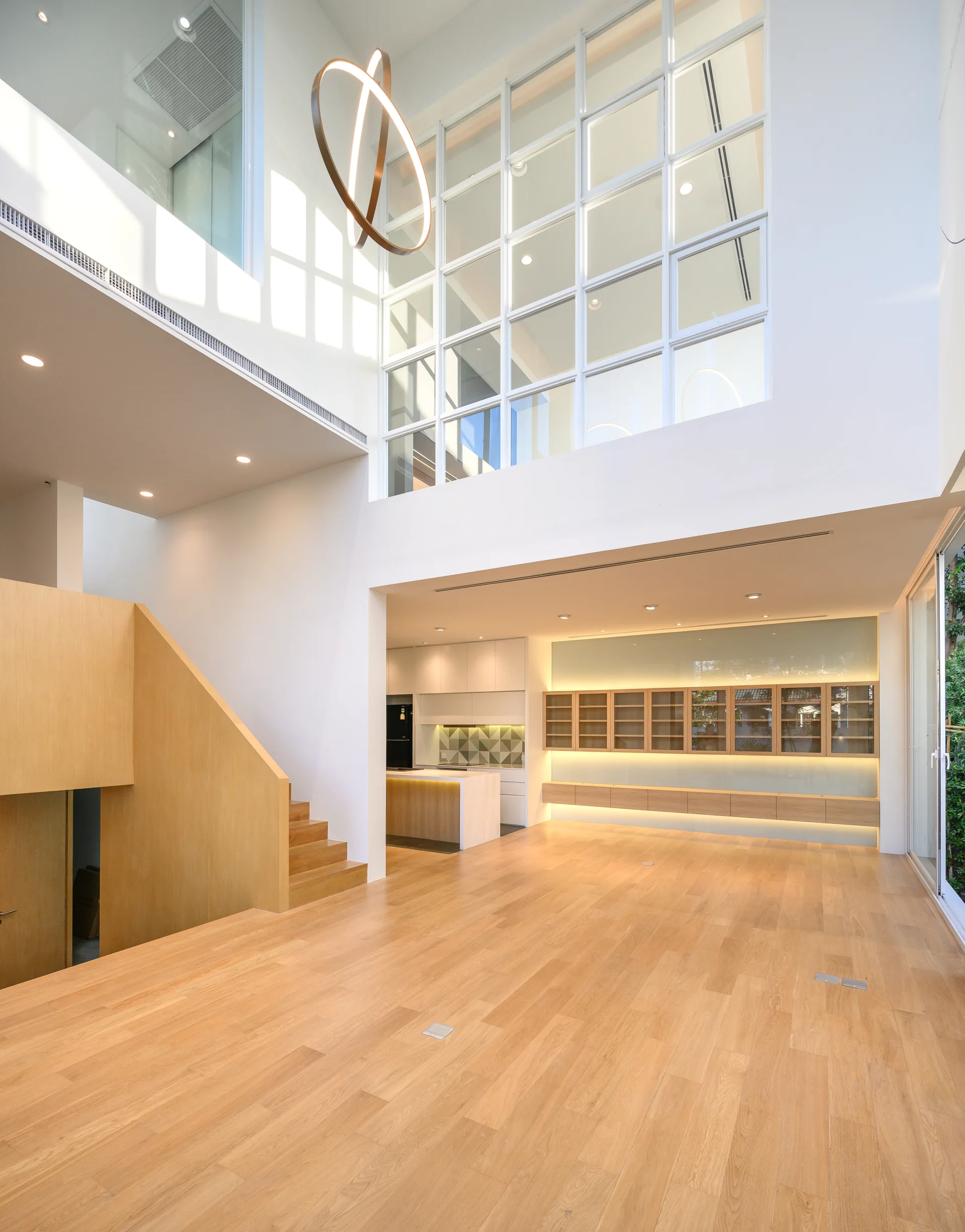 A double-height modern living space features light wood flooring, a matching wooden staircase, and a large grid window overlooking the upper level.