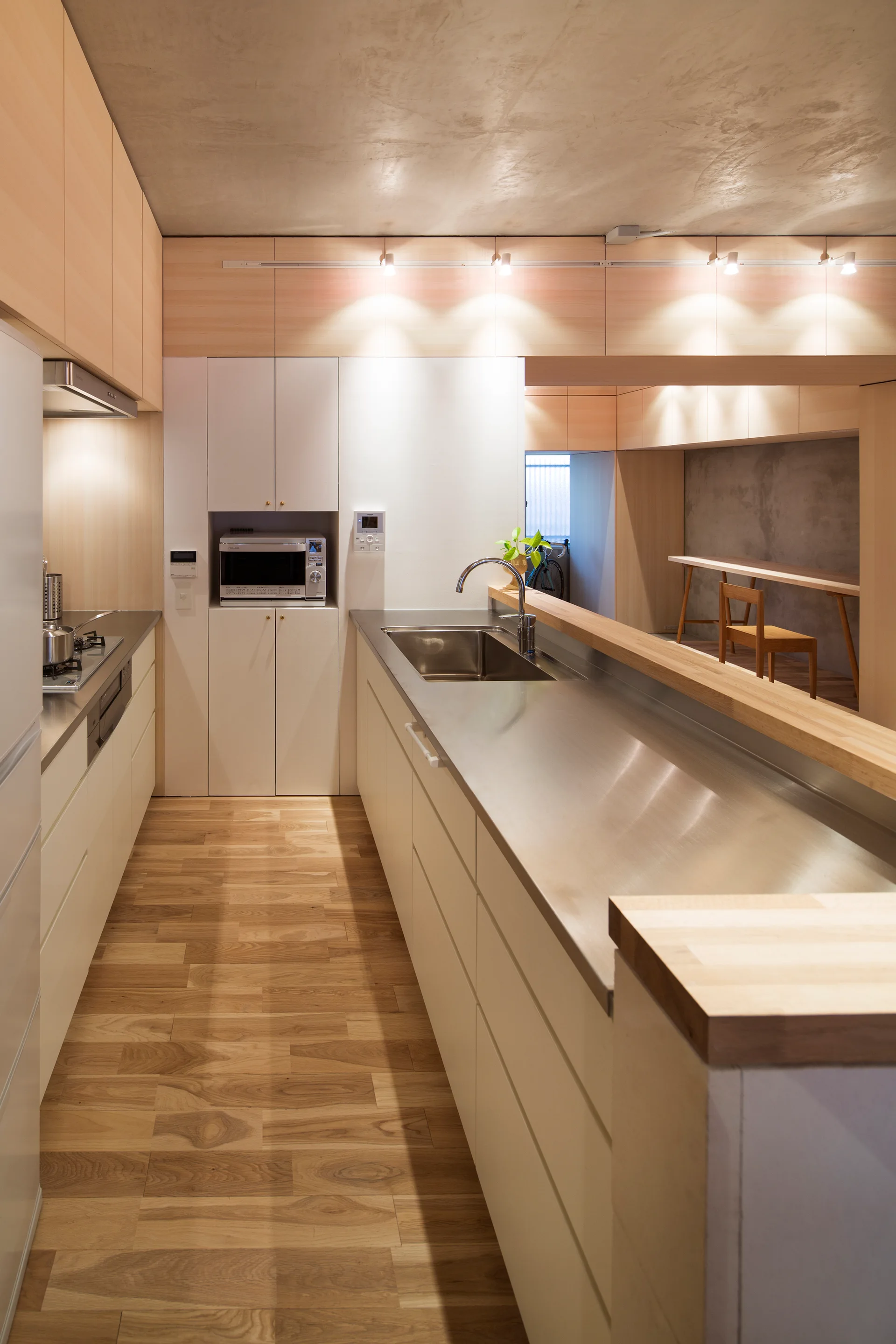 A modern galley kitchen featuring a stainless steel island, flat-panel wood cabinets, and an exposed raw concrete ceiling.