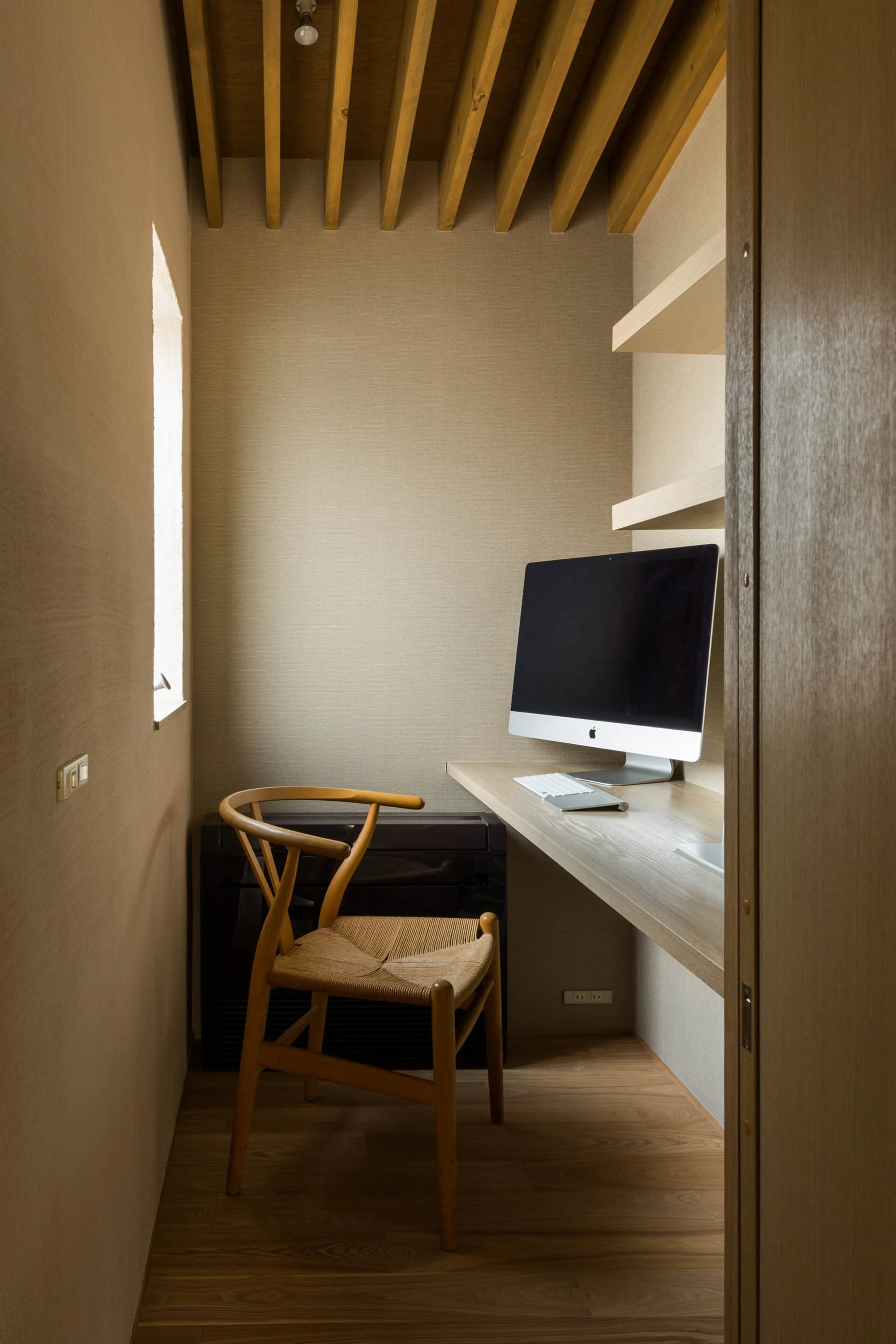 A small home office alcove featuring a floating wooden desk, a classic wooden chair, floating shelves, and a slatted wood ceiling.