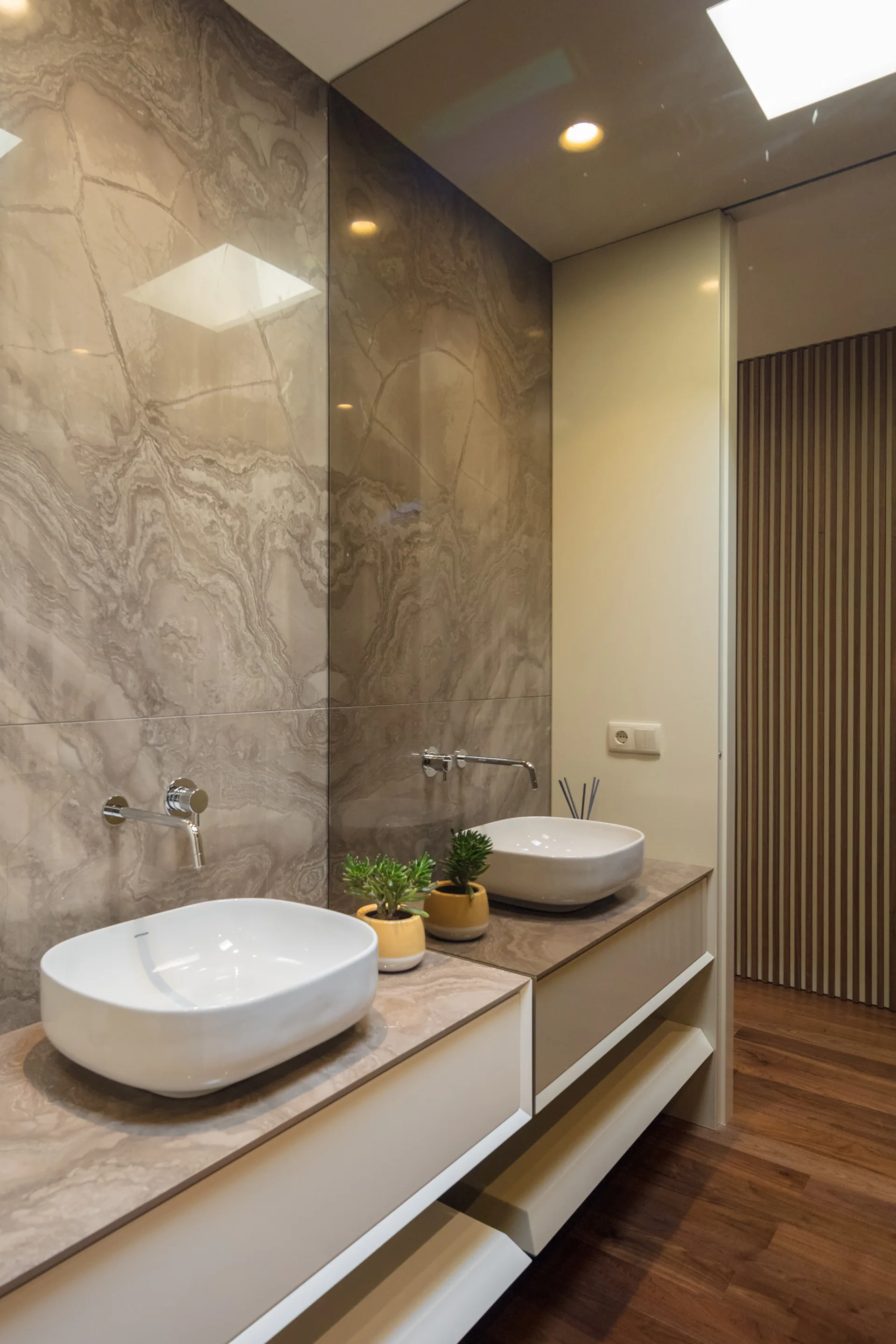 A modern bathroom vanity with a white vessel sink on a stone countertop, featuring a large mirror that reflects the veined stone wall.