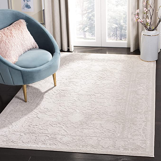 A blue velvet barrel-style armchair with a pink fuzzy pillow sits on a large ivory patterned area rug over dark wood flooring.