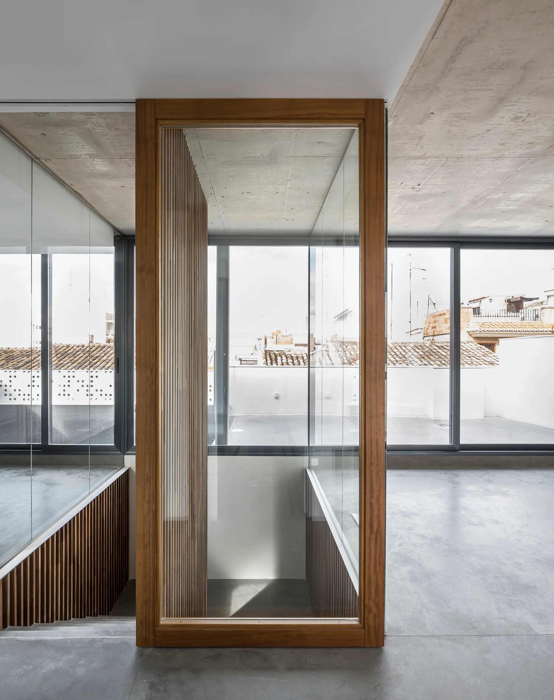 A minimalist room featuring a glass-enclosed staircase framed in wood with a concrete ceiling and floor.