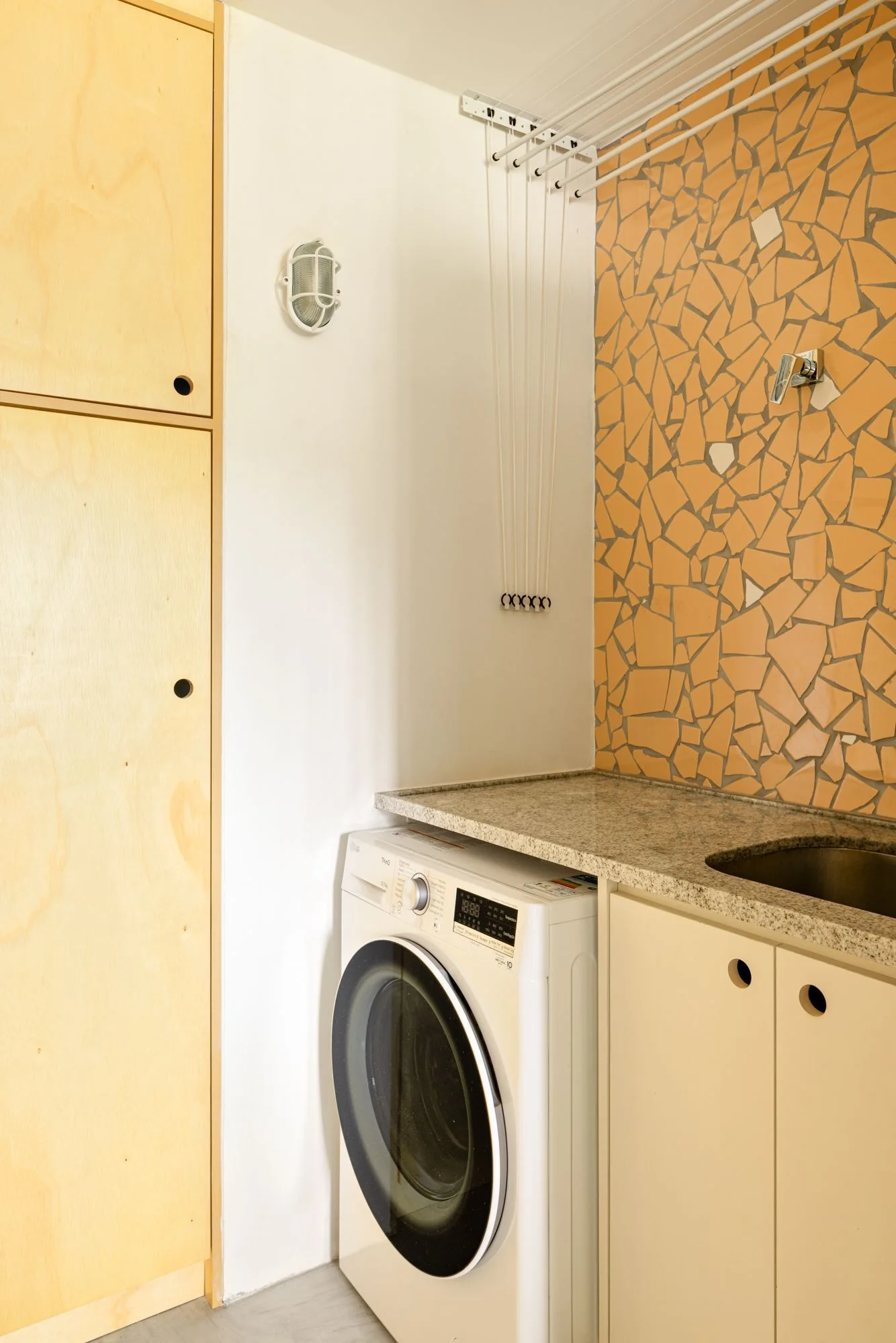 A utility laundry room featuring light wood cabinets, an orange mosaic tile backsplash, and a front-loading washing machine.