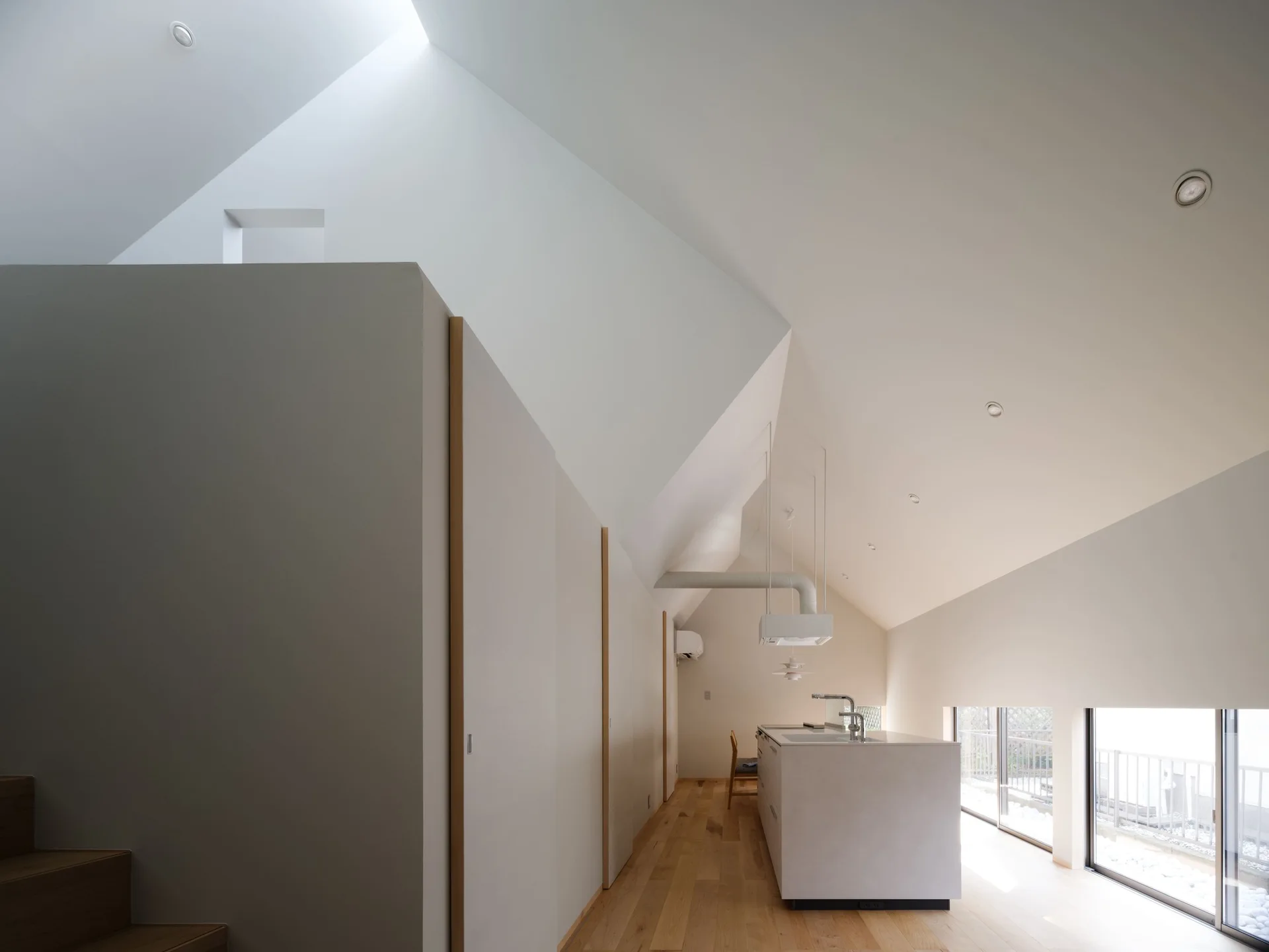 A minimalist white kitchen featuring a central island, light wood flooring, flush cabinetry, and a high vaulted ceiling with a skylight.