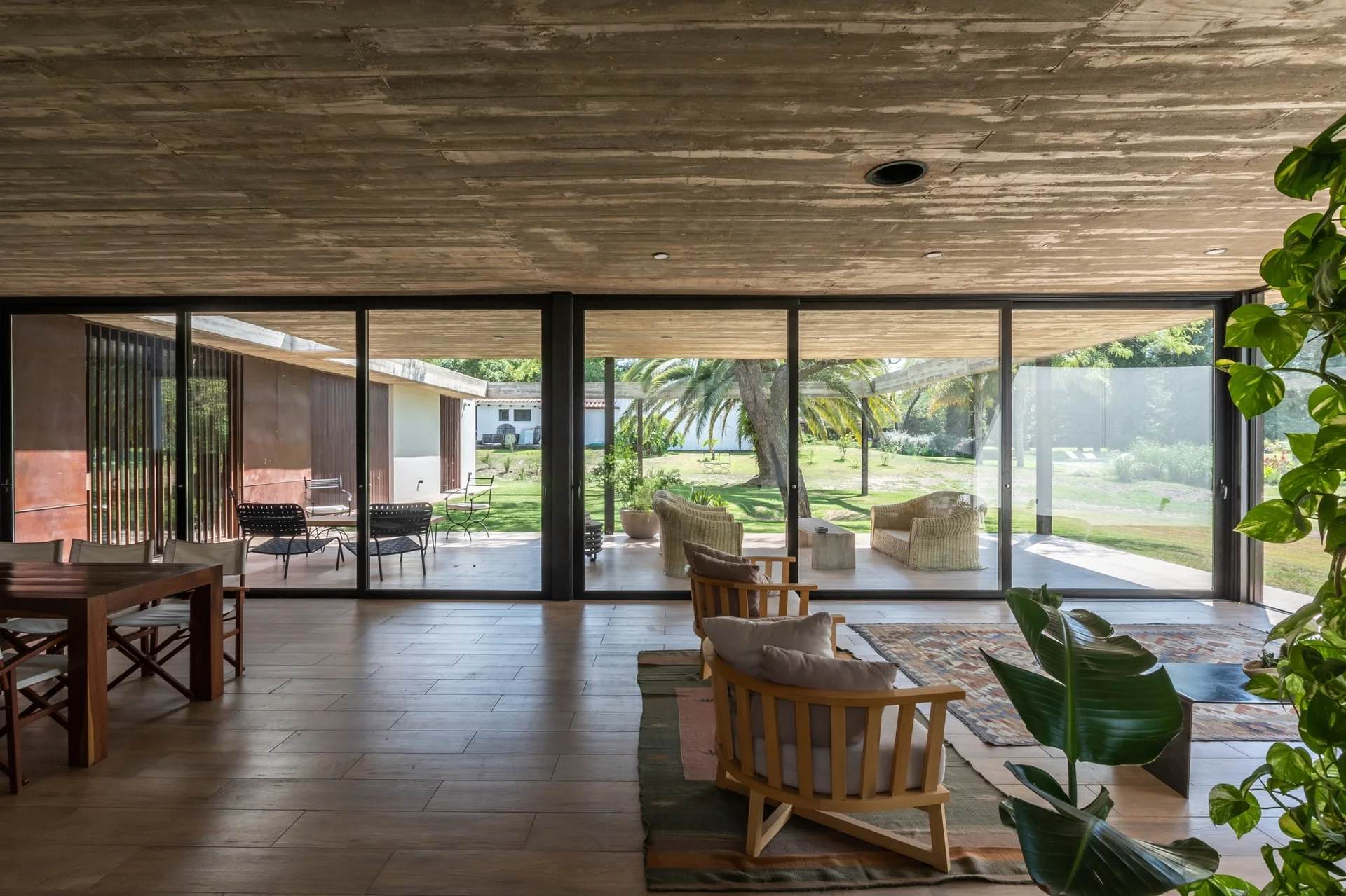 A modern living space features a board-formed concrete ceiling, wood flooring, and sliding glass doors opening to a grassy patio.