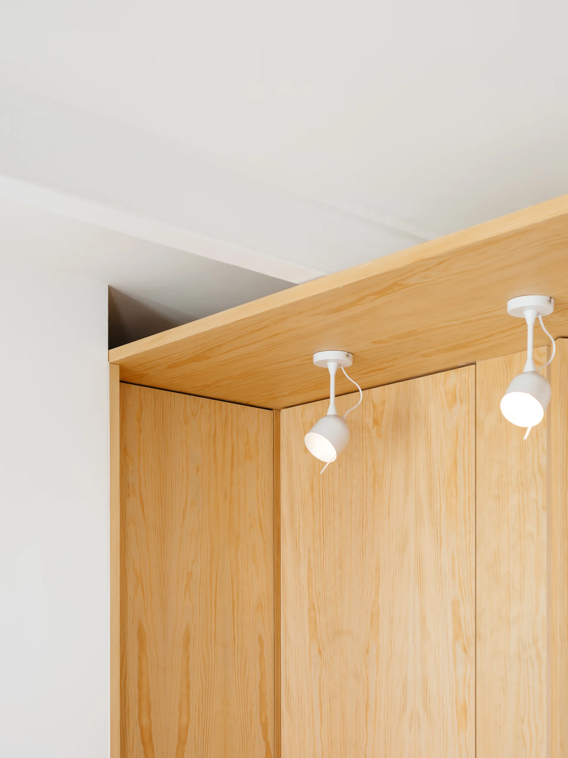 A close-up of custom light wood cabinetry with two integrated white spotlights mounted on a matching wooden overhang against a white wall.