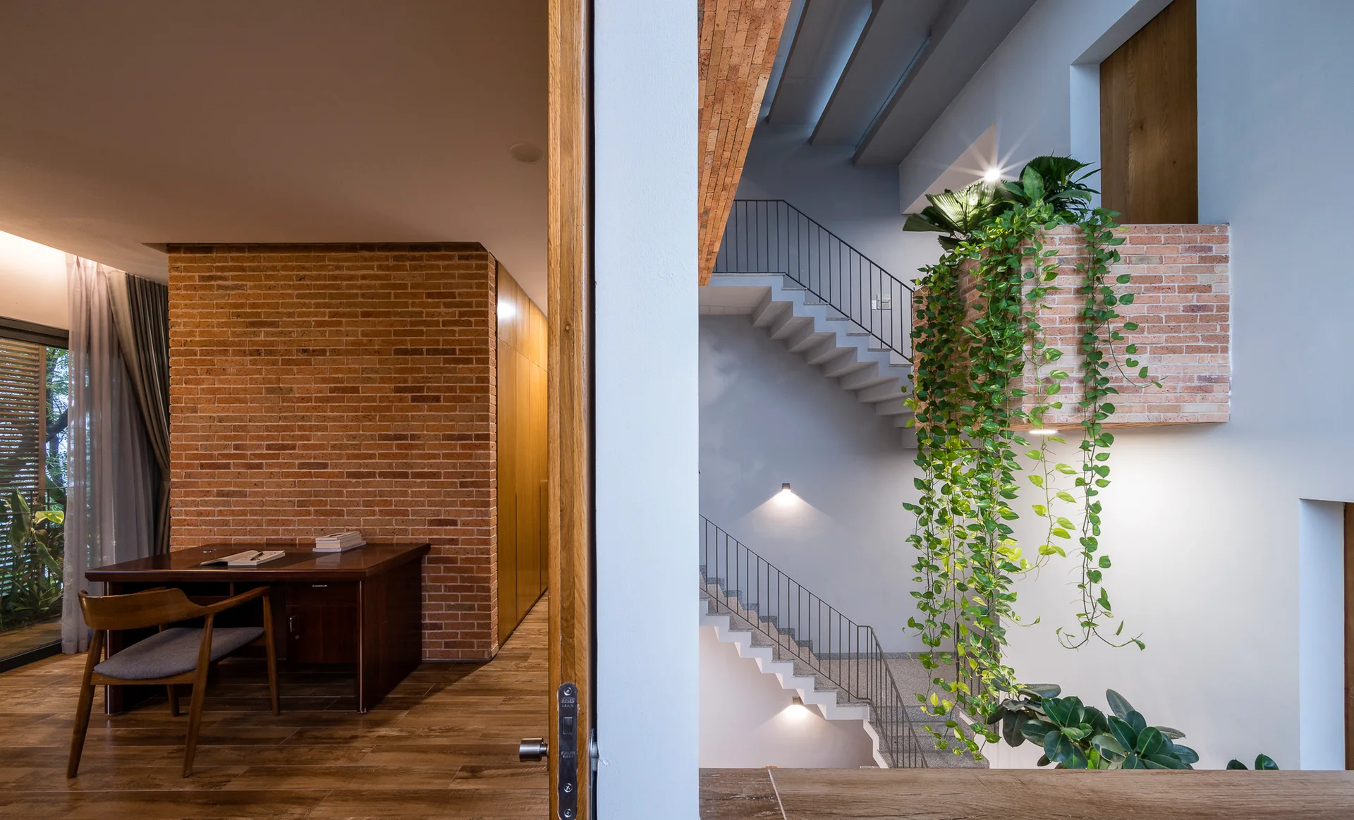 A modern home office with a wood desk looks out to a concrete staircase featuring an exposed brick planter with cascading green plants.