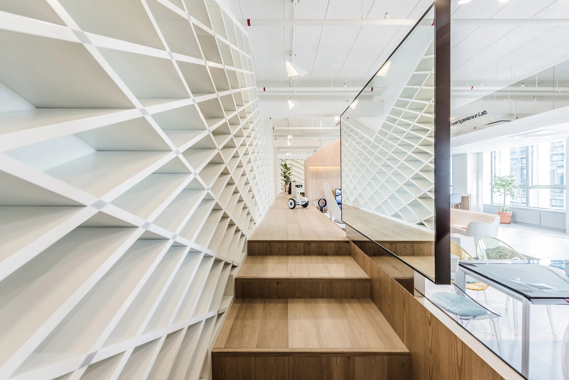 A modern minimalist interior featuring a white diamond grid shelving wall, wooden staircase, and a large mirror.