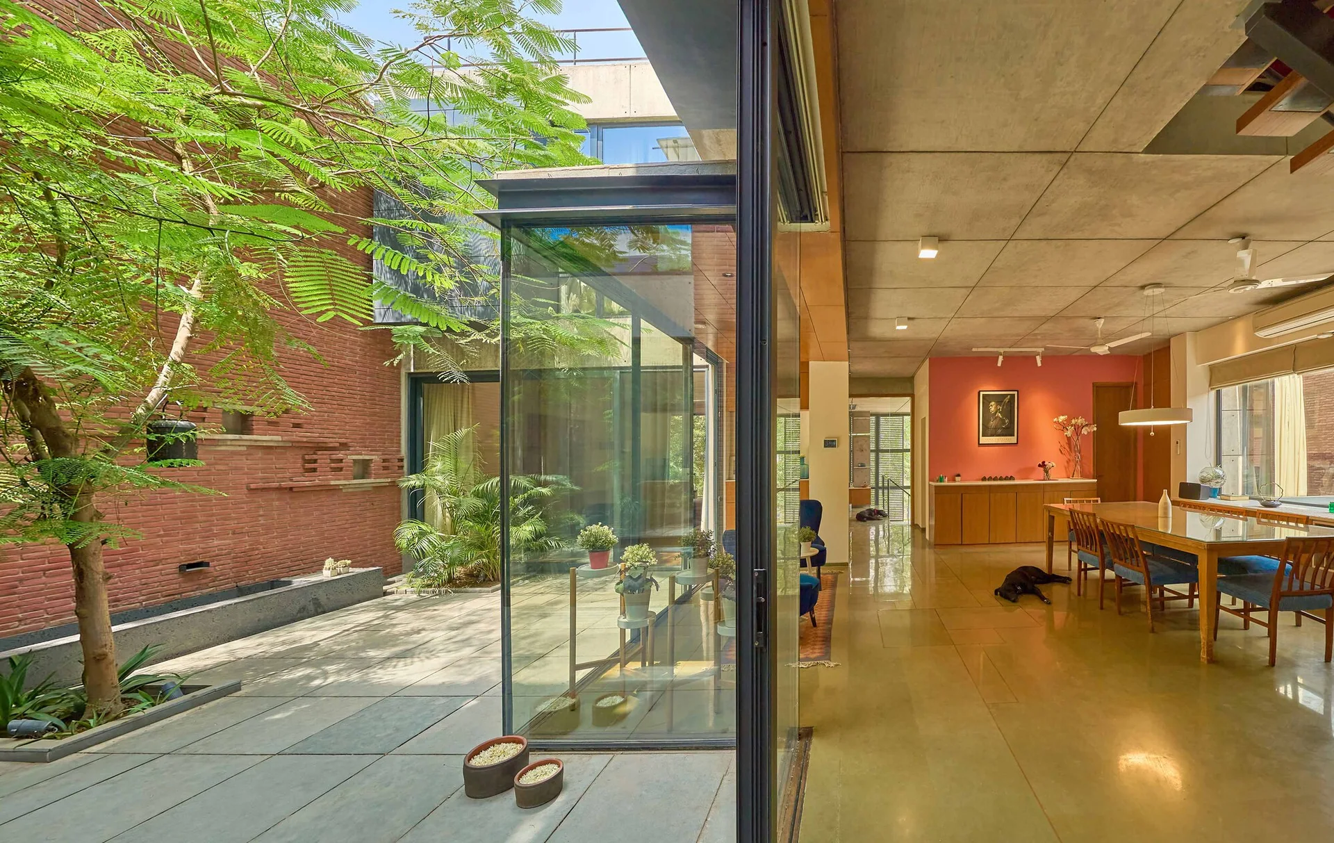 A contemporary dining room with a long wooden table, exposed concrete ceiling, and sliding glass doors that open to a brick courtyard.