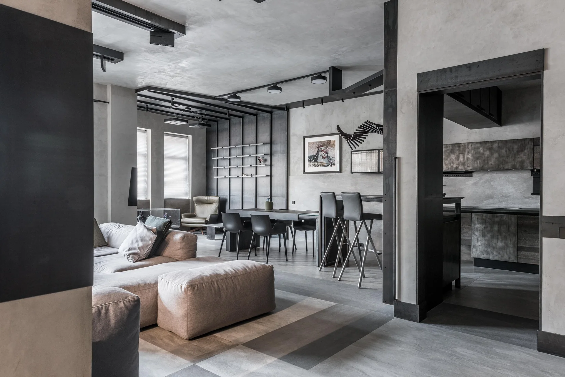 An industrial open-concept living room features a modular grey sectional sofa, concrete-textured walls, black steel ceiling beams, and a dining area.