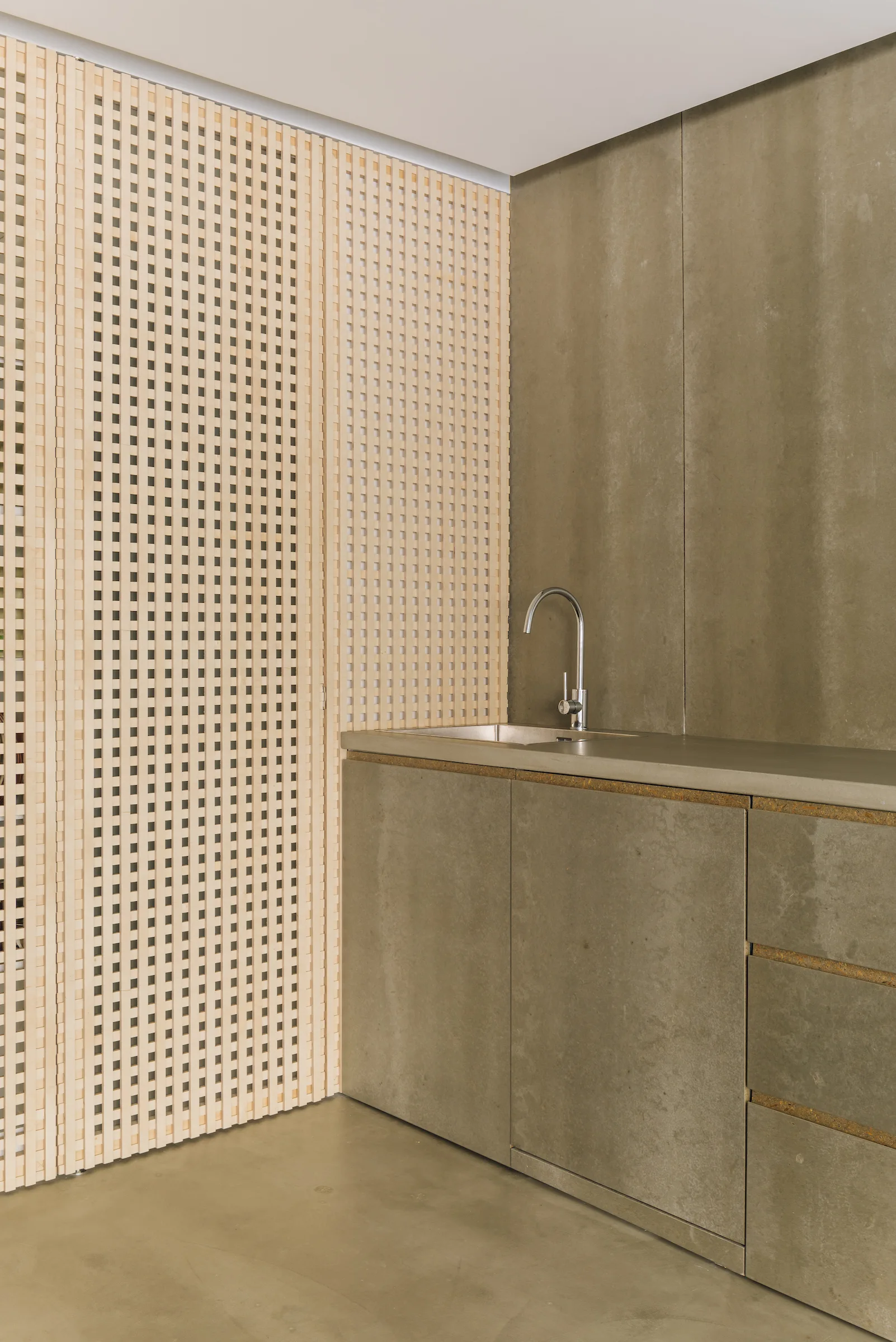 A grey concrete-look vanity with a chrome faucet stands next to a decorative light wood lattice wall panel.