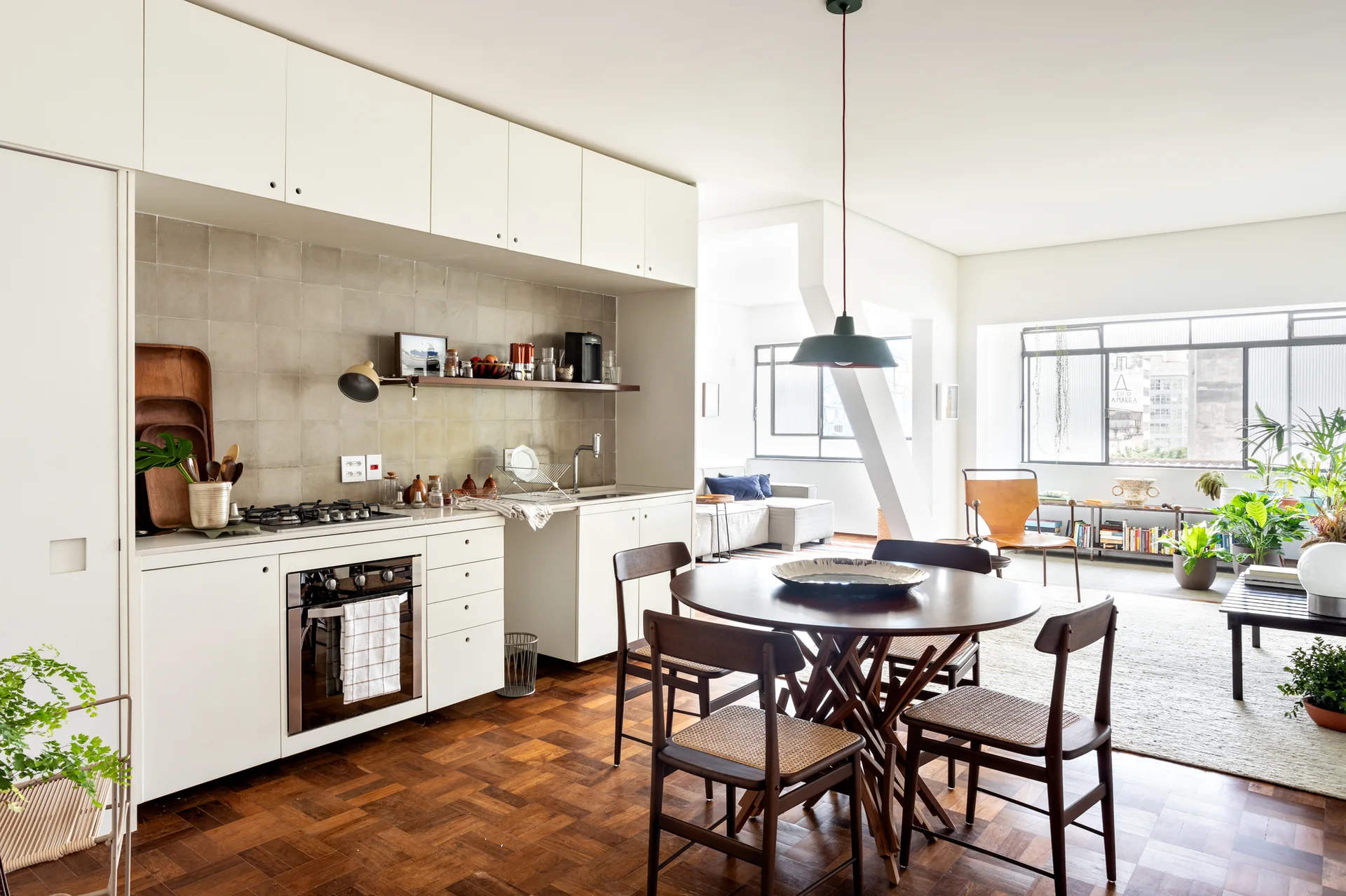 An open-concept kitchen and dining area features minimalist white cabinets, a gray tile backsplash, parquet flooring, and a round dark wood table.