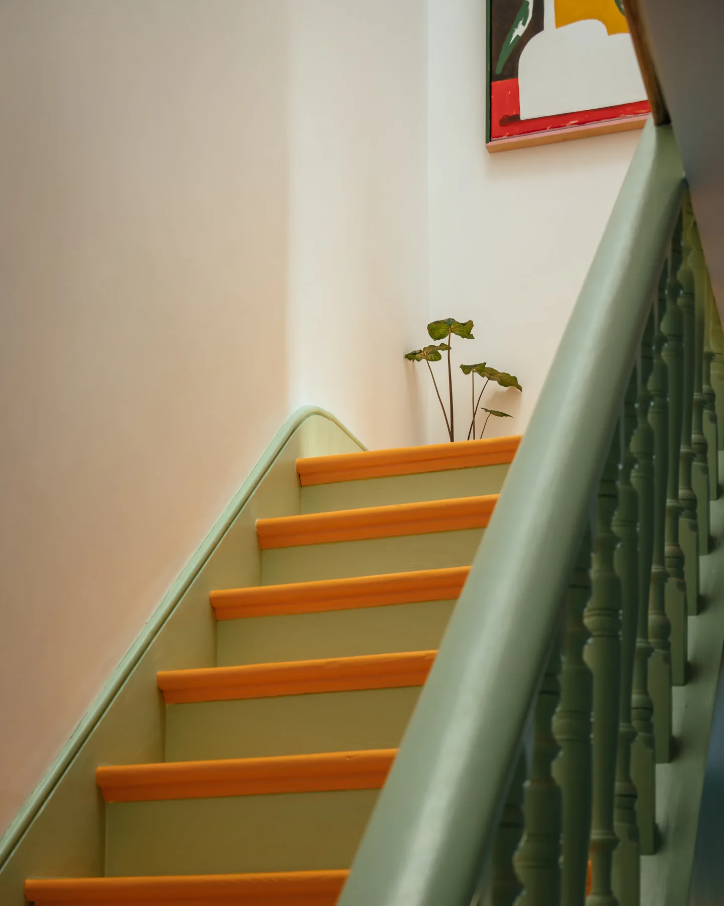 A close-up of a wooden staircase featuring sage green risers and balustrade paired with bright yellow treads against an off-white wall.