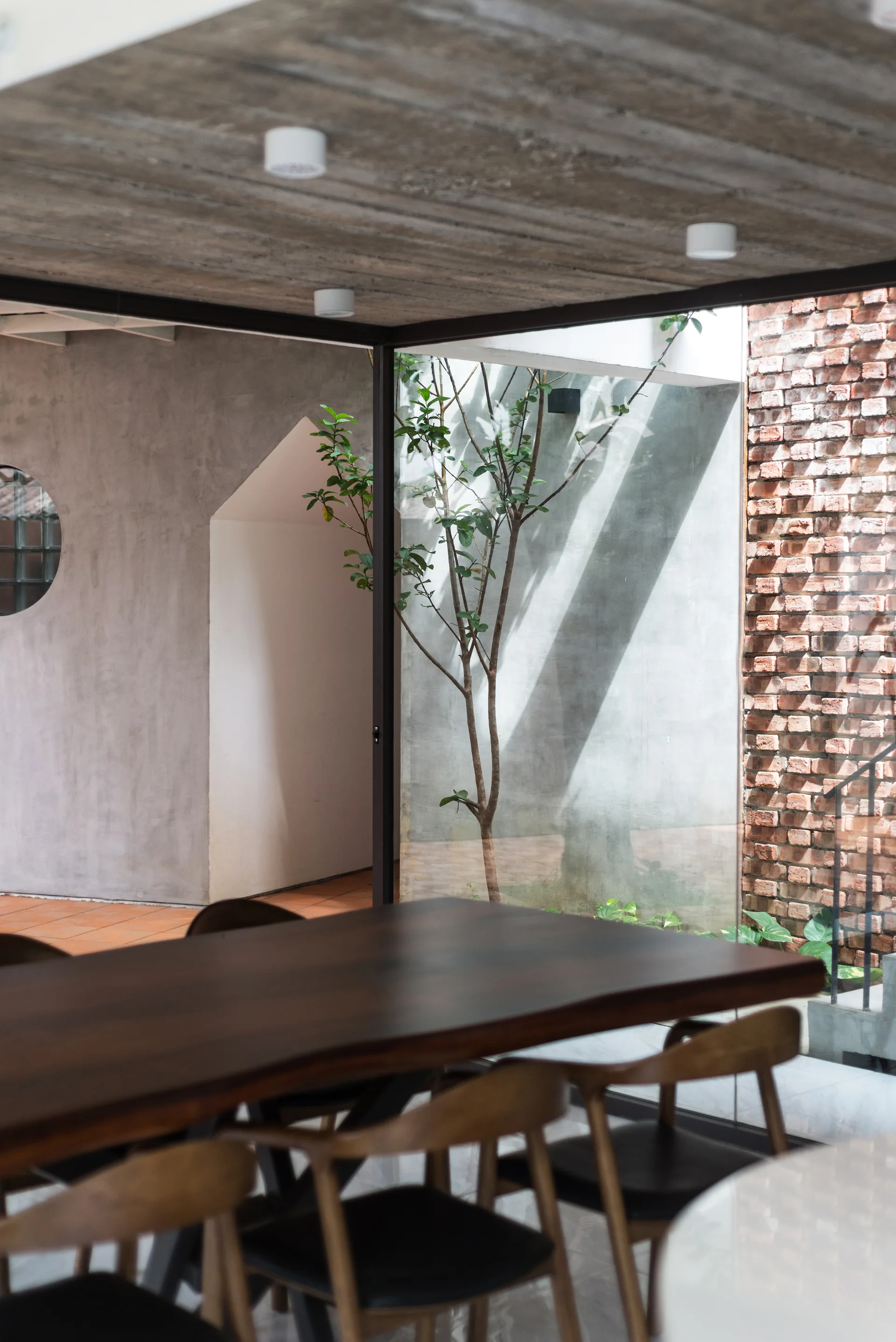 A modern dining room features a dark wood table and chairs situated next to a glass wall overlooking an outdoor brick courtyard.