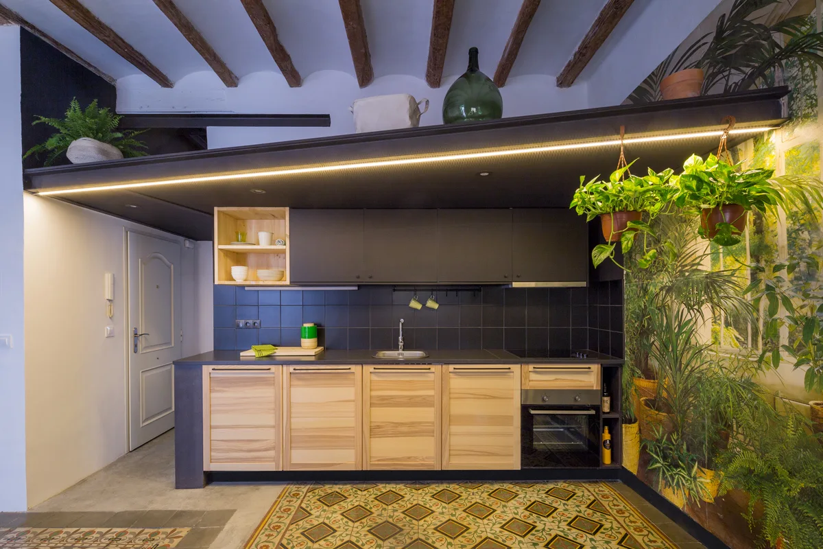 A kitchen with light wood lower cabinets, matte black upper cabinets, a dark tile backsplash, exposed ceiling beams, and patterned floor tiles.