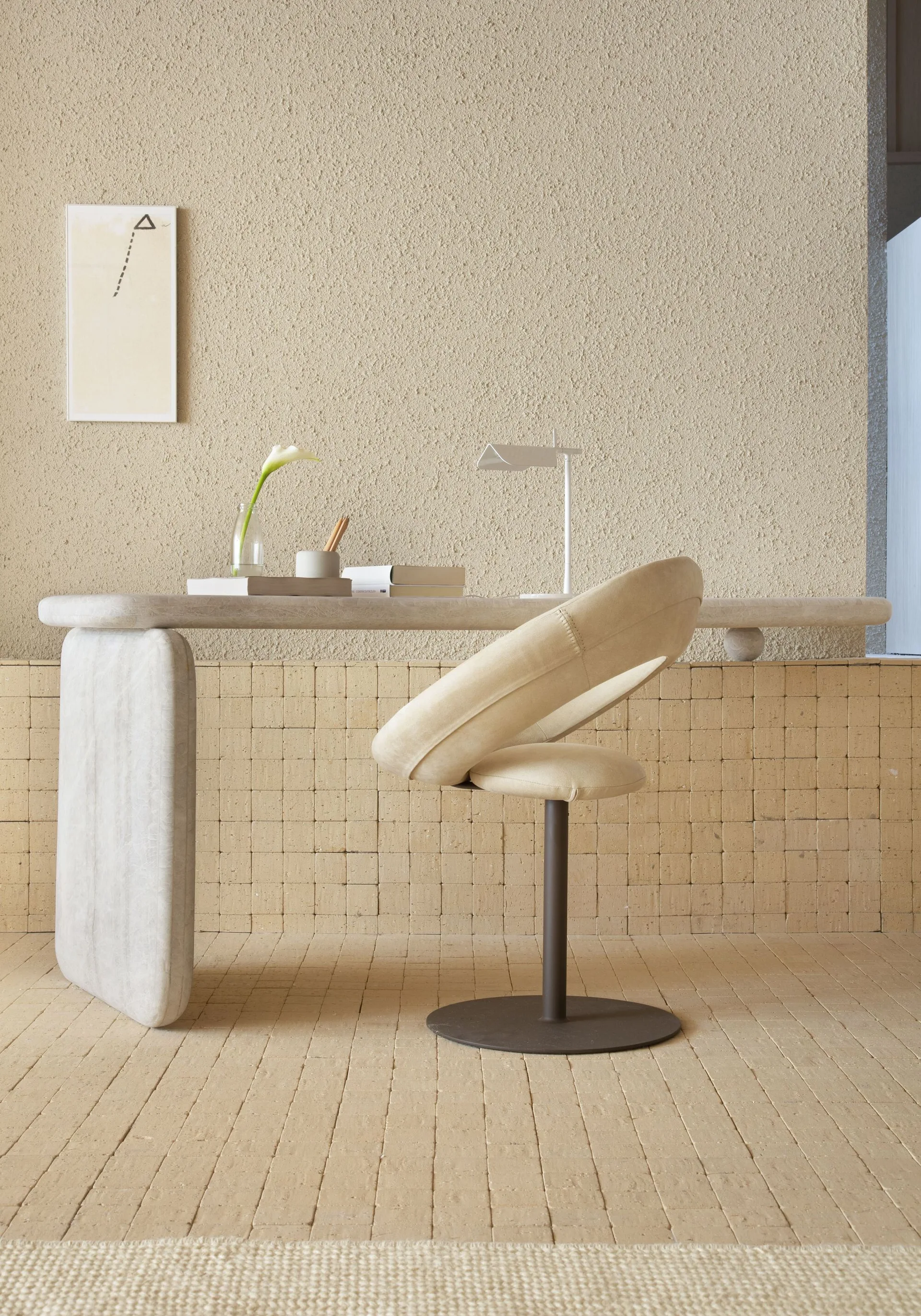 A minimalist home office workspace features a sculptural stone desk, a curved beige swivel chair, and a highly textured plaster wall.