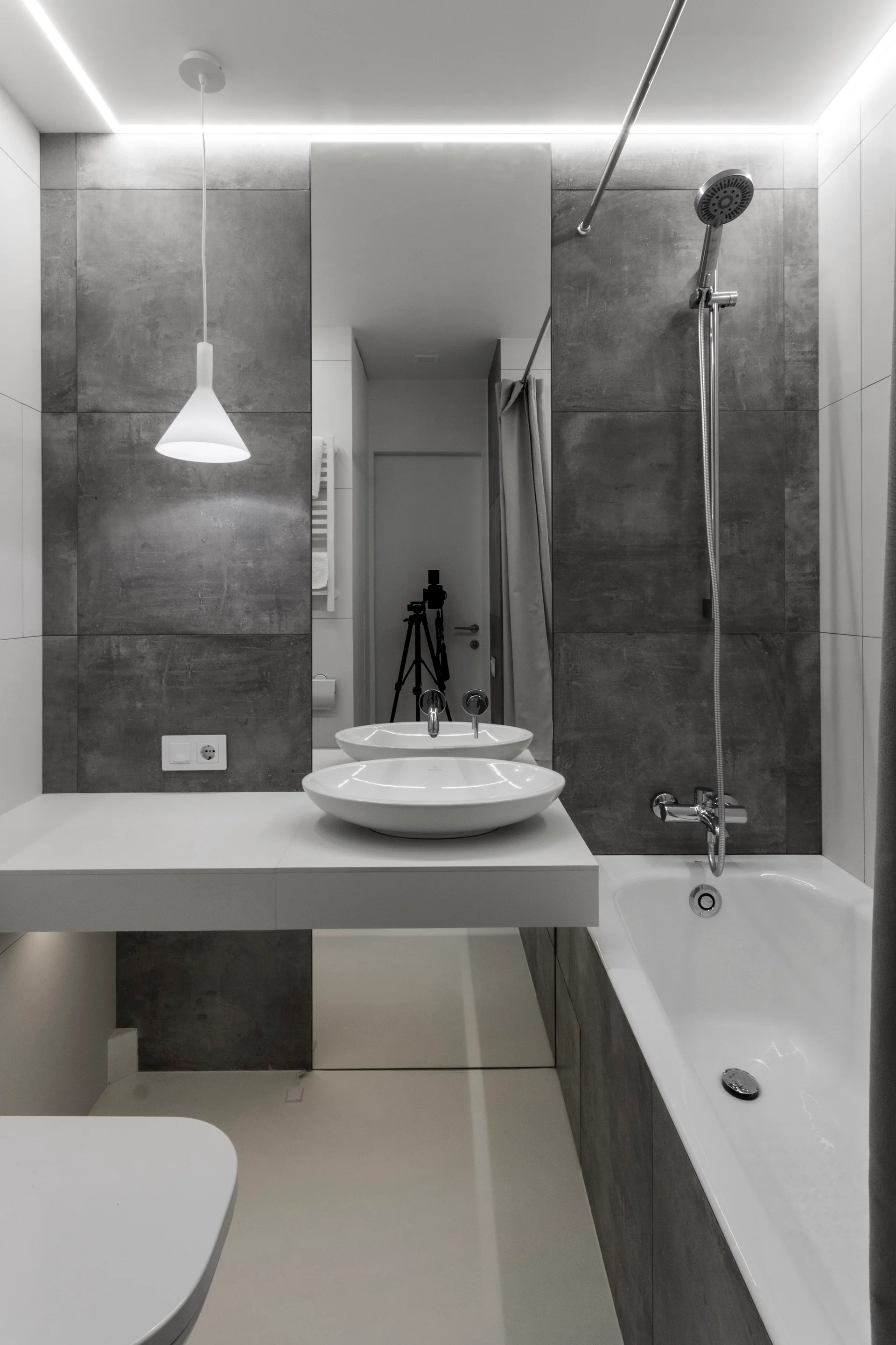 A modern bathroom with dark grey wall tiles, a white floating vanity counter with a vessel sink, and an integrated bathtub.