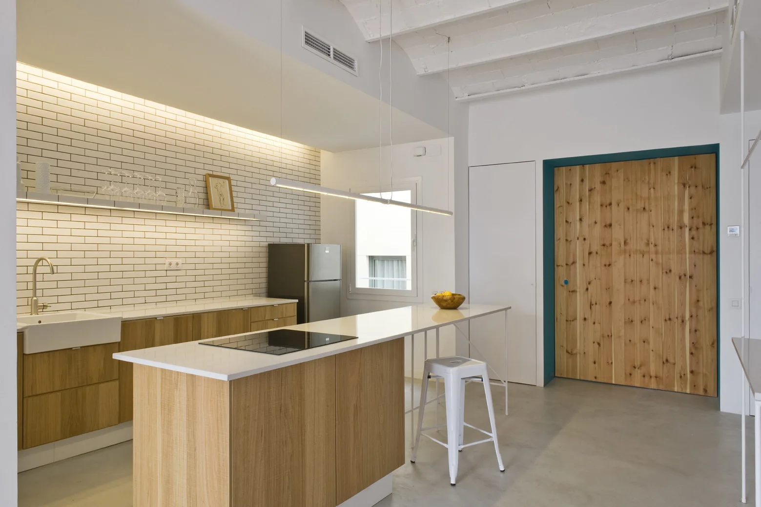 A modern Scandinavian kitchen features light wood cabinets, a white subway tile backsplash, a long island, and a sliding wooden door.