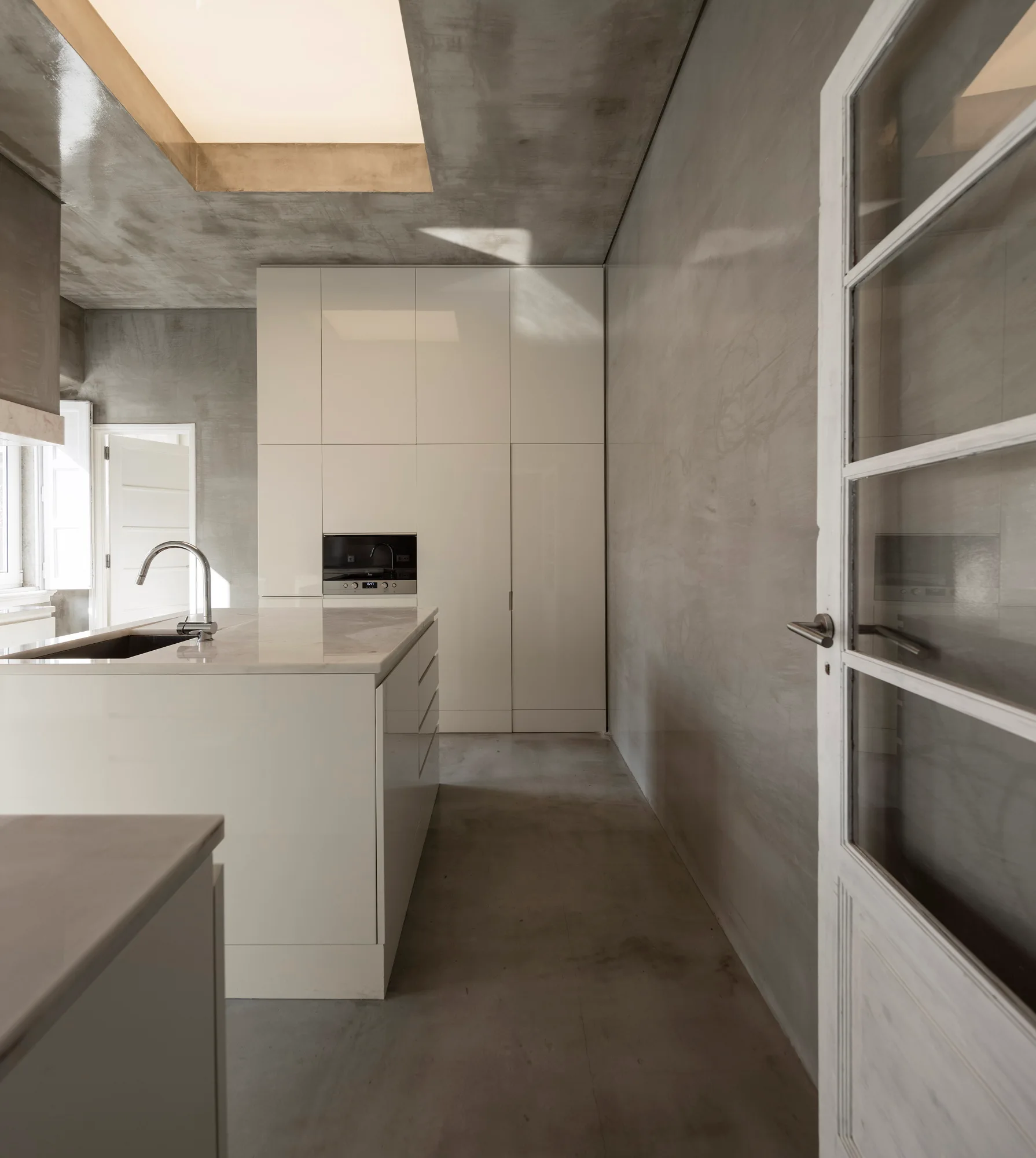 A minimalist gray concrete kitchen with seamless glossy white cabinetry, a central kitchen island, and an overhead skylight.