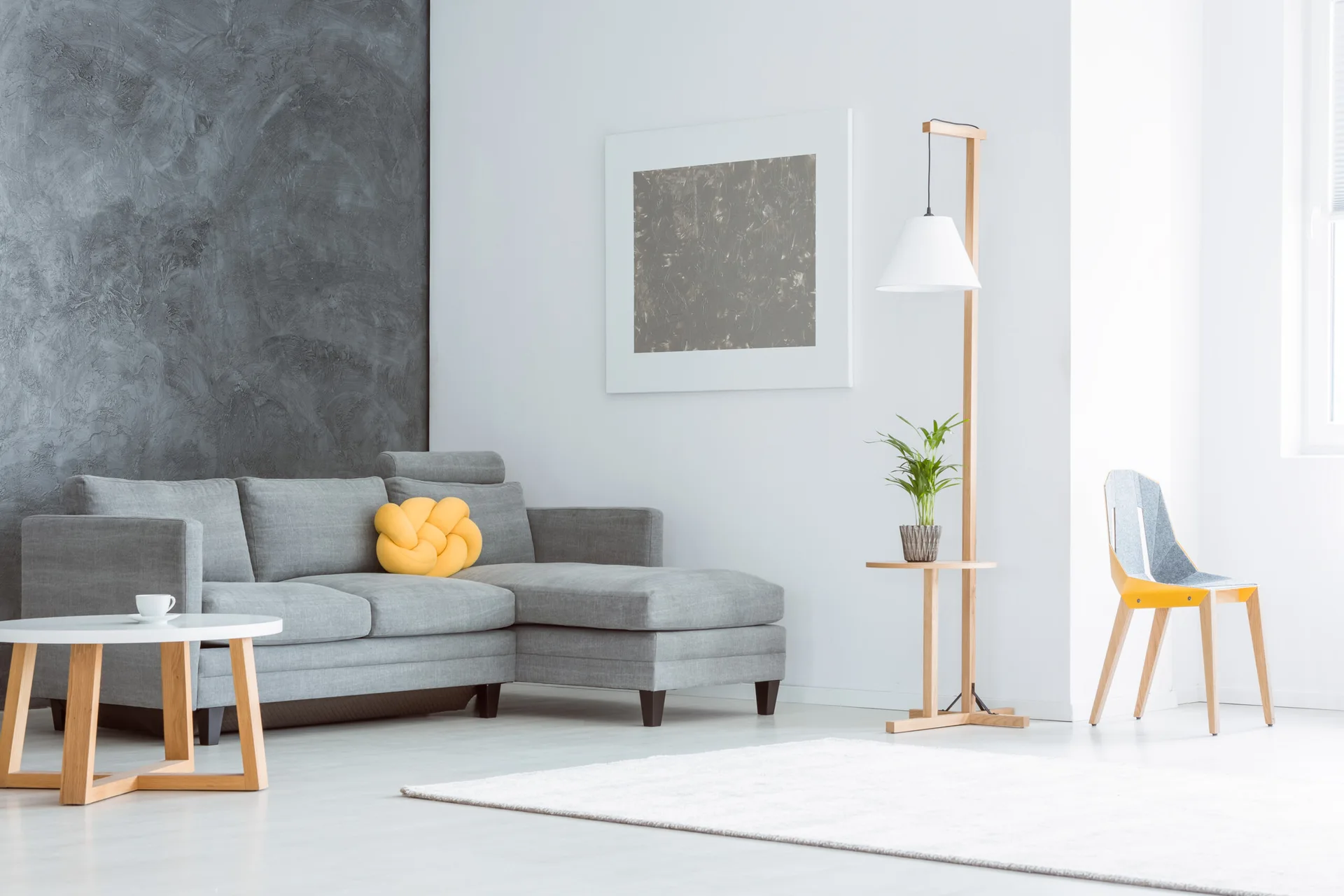 A modern living room features a gray sectional sofa next to a textured dark gray wall, a light wood floor lamp, and a yellow knot pillow.