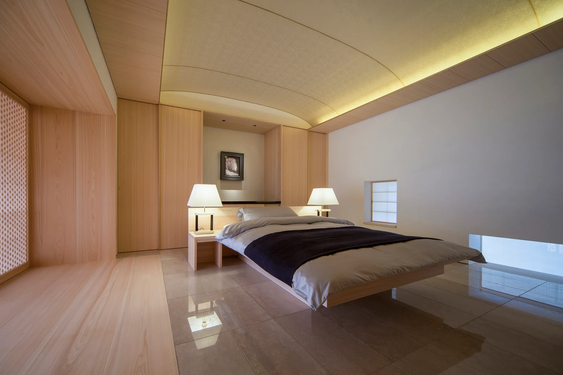 A minimalist bedroom features a floating platform bed, light wood paneling, a curved cove-lit ceiling, and glossy beige tiled floors.