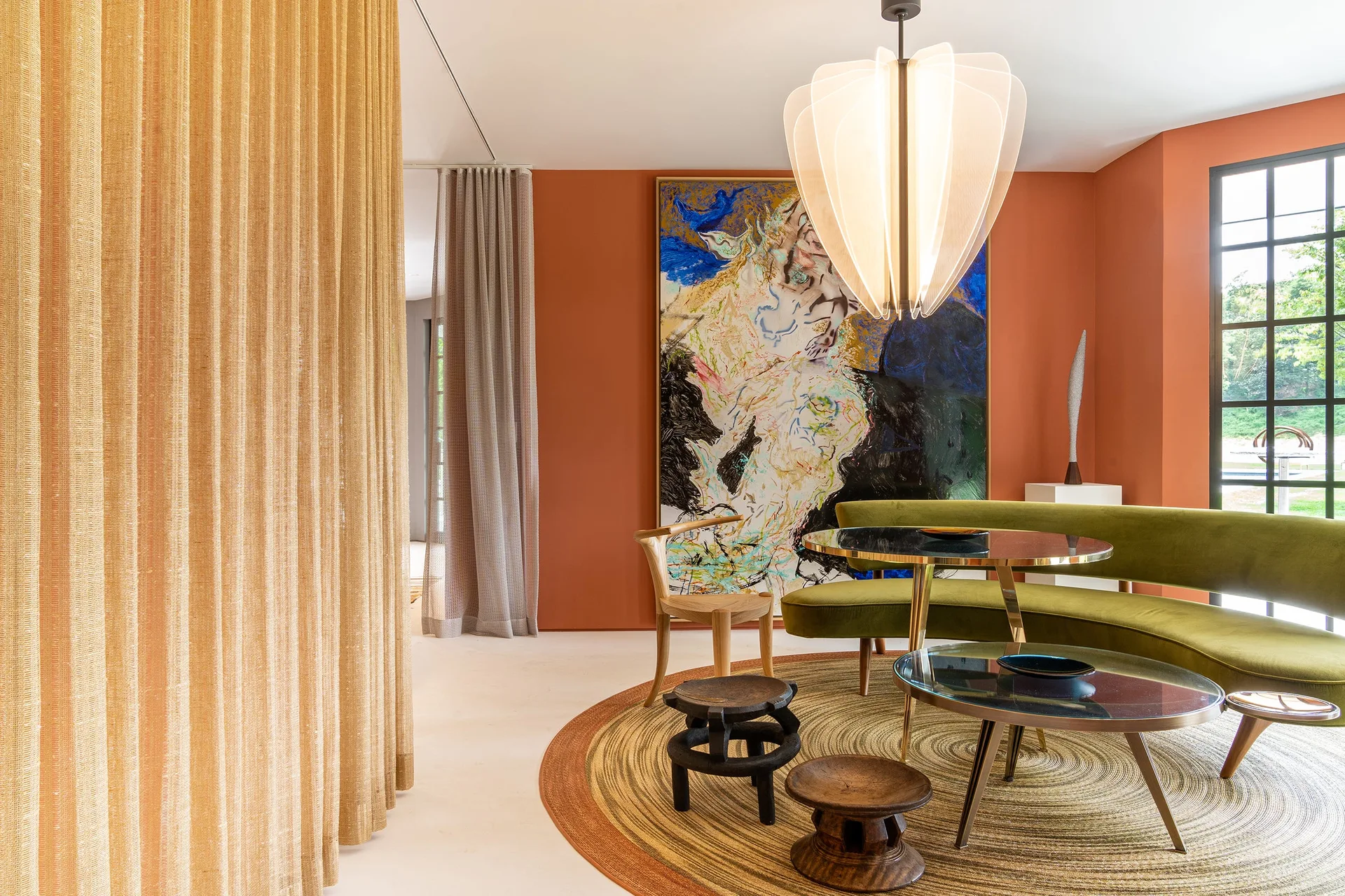 A curved olive green sofa sits on a circular woven rug in a living room with terracotta walls and glass coffee tables.