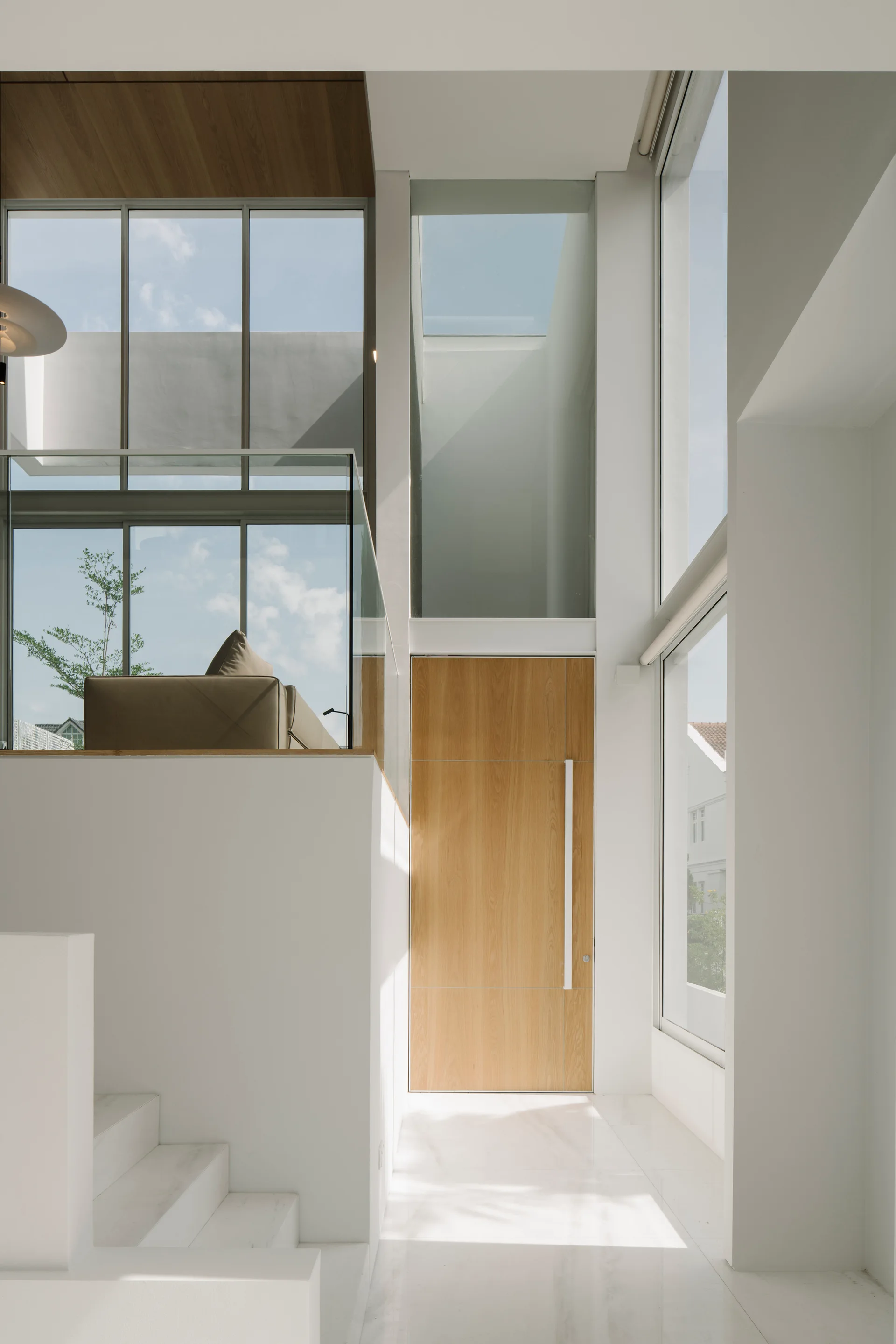 A double-height modern foyer features a large wooden entry door, white marble floors, a white staircase, and a mezzanine with a glass railing.