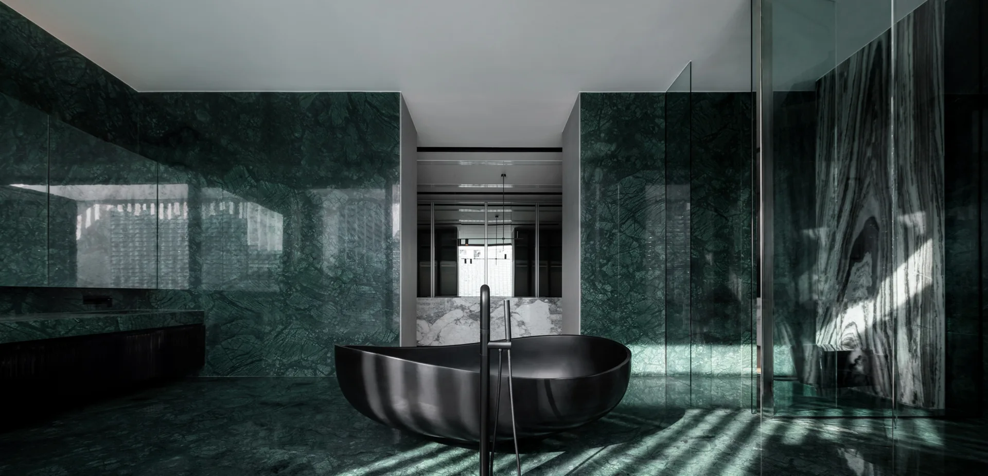 A modern bathroom clad in polished dark green veined marble features a sculptural matte black freestanding bathtub and glass partitions.