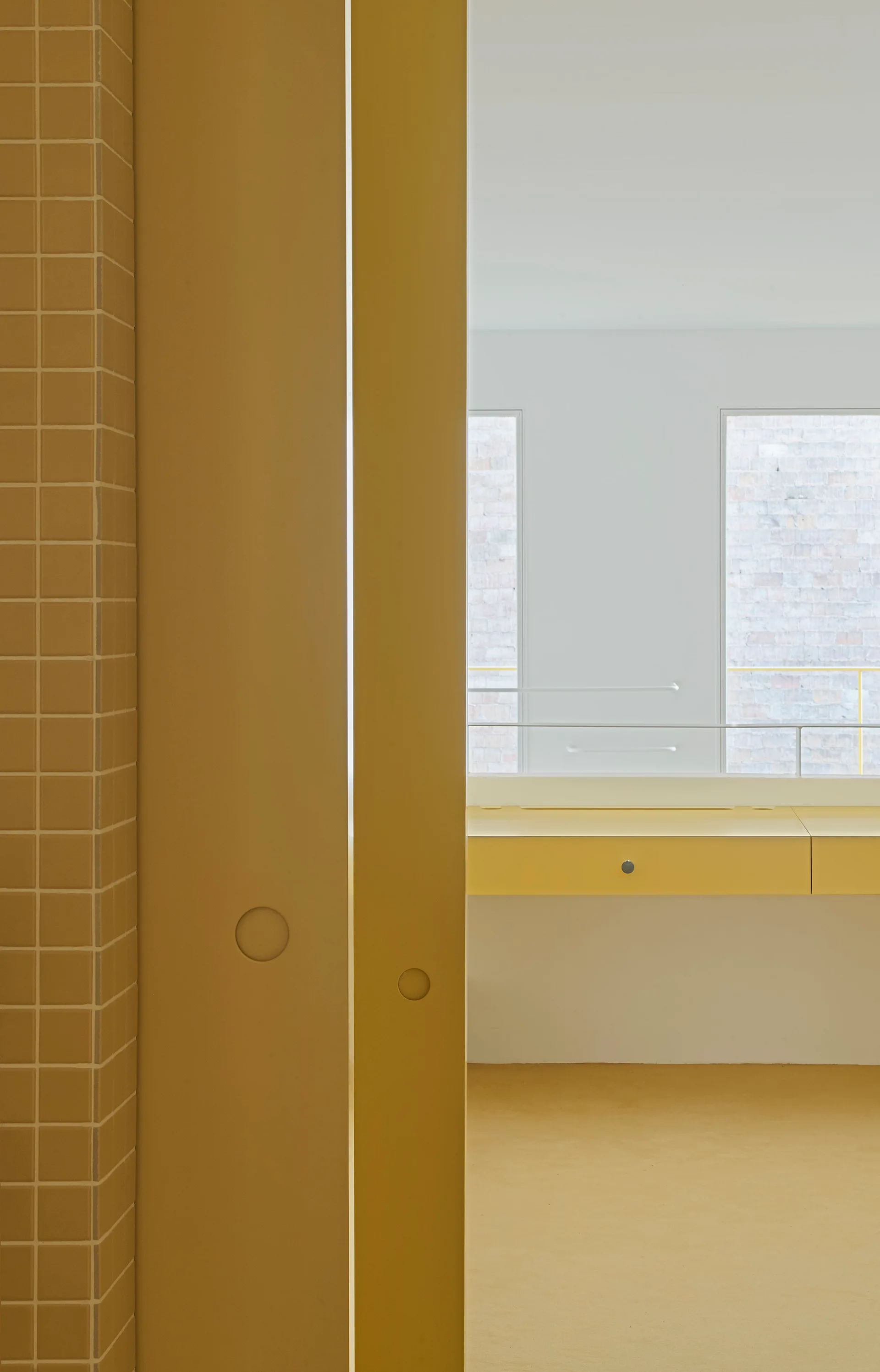 A minimalist yellow bathroom features a square-tiled wall, a solid yellow sliding door, and a matching wall-mounted vanity in the background.