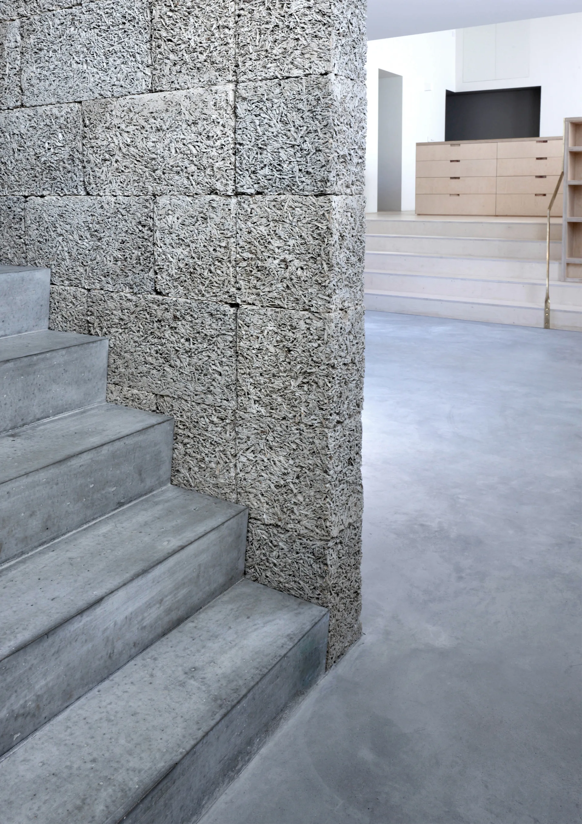 Smooth concrete stairs ascend next to a highly textured grey block wall with light wood built-in drawers visible in the background.