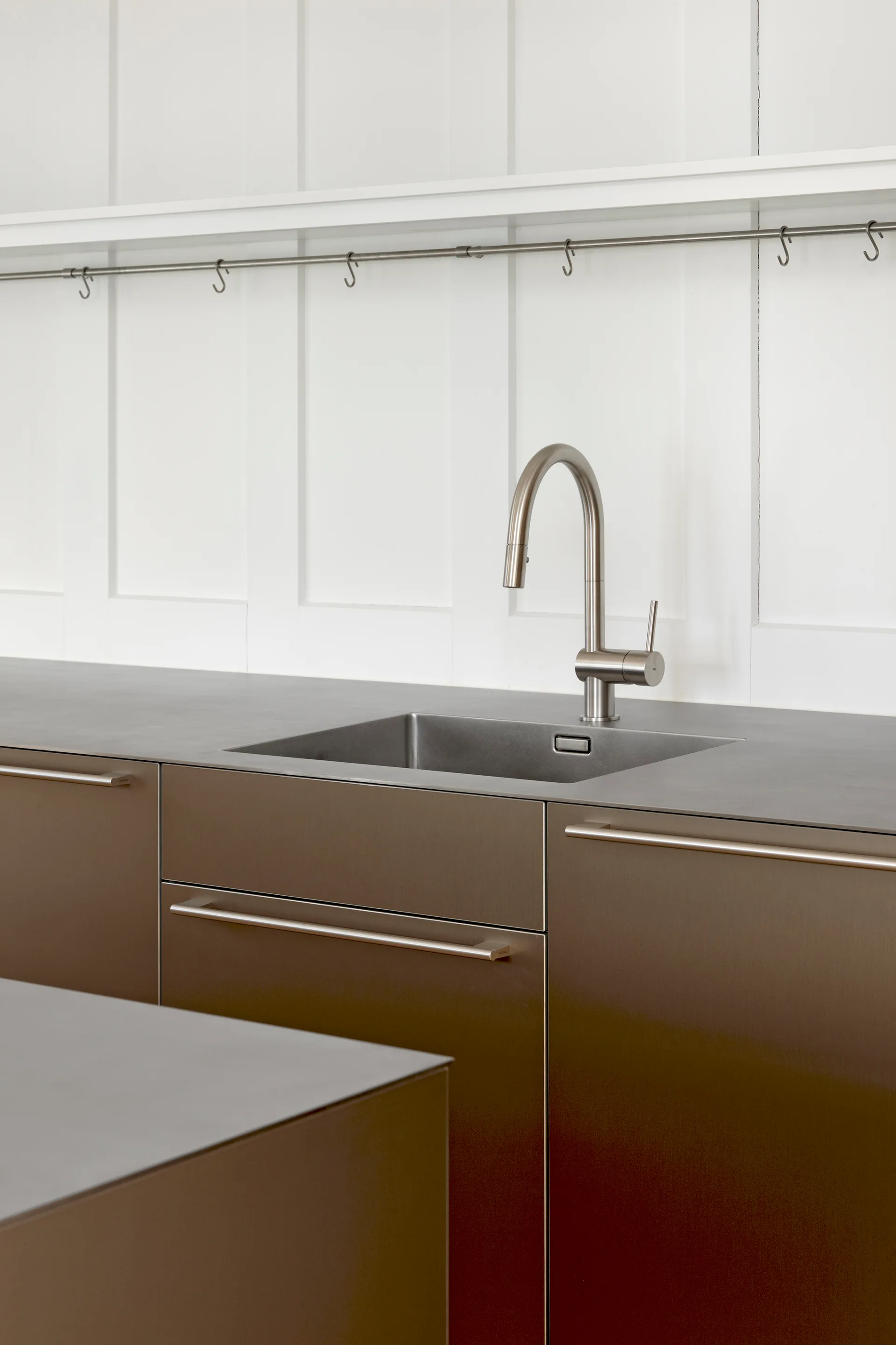 A modern kitchen workspace with brushed bronze cabinets, a dark matte countertop with an undermount sink, and white vertically paneled walls.