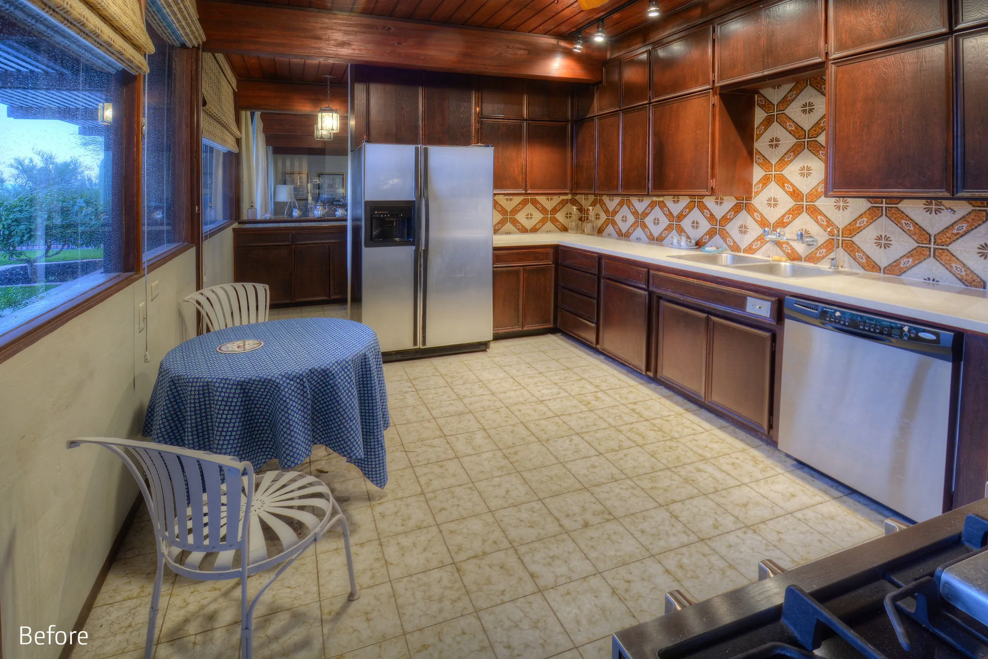 A rustic kitchen featuring dark wood cabinetry, a patterned orange and white tile backsplash, and a dining table with a blue patterned tablecloth.