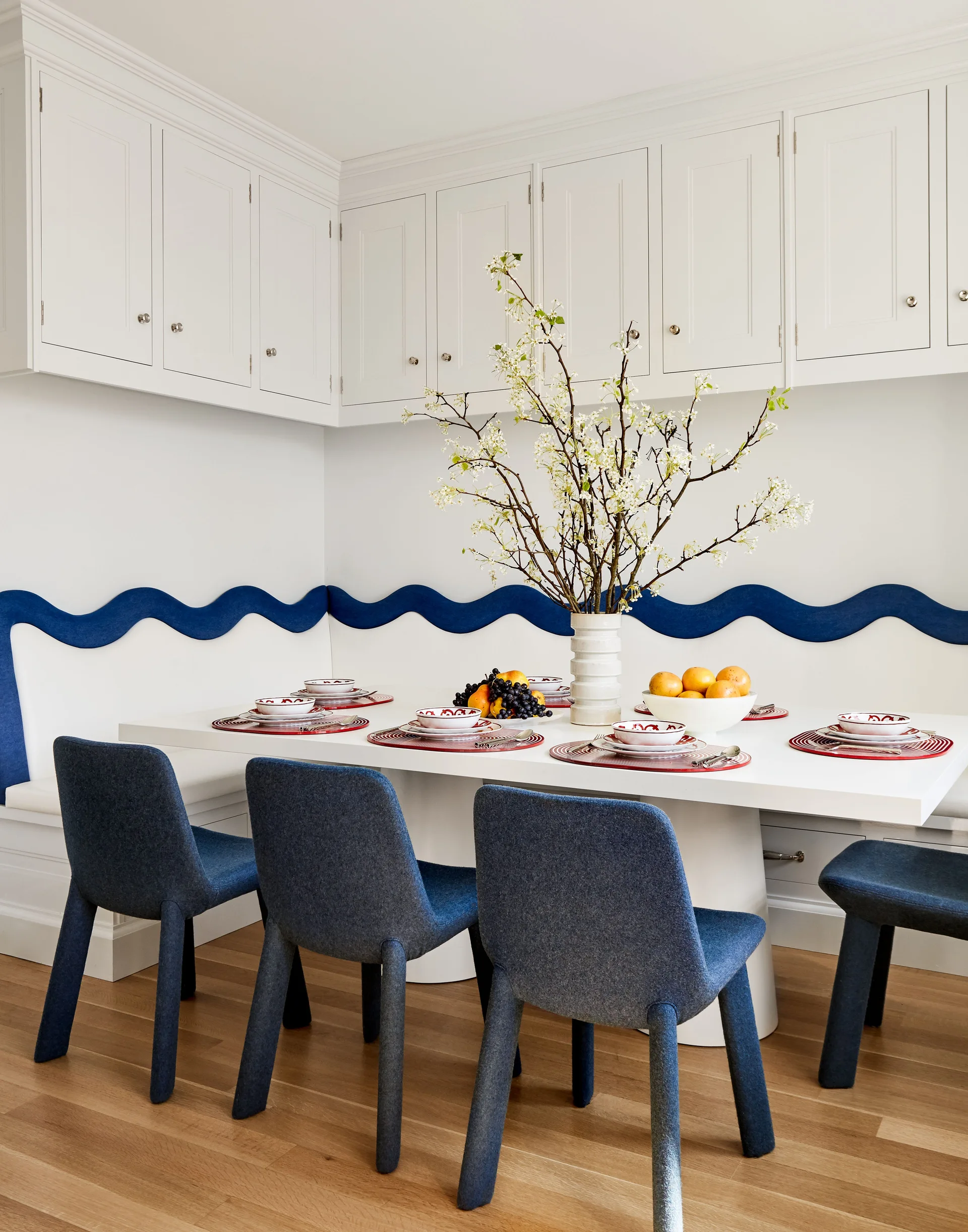 A bright breakfast nook features a white table, blue upholstered chairs, and a white built-in banquette with a wavy blue accent stripe.