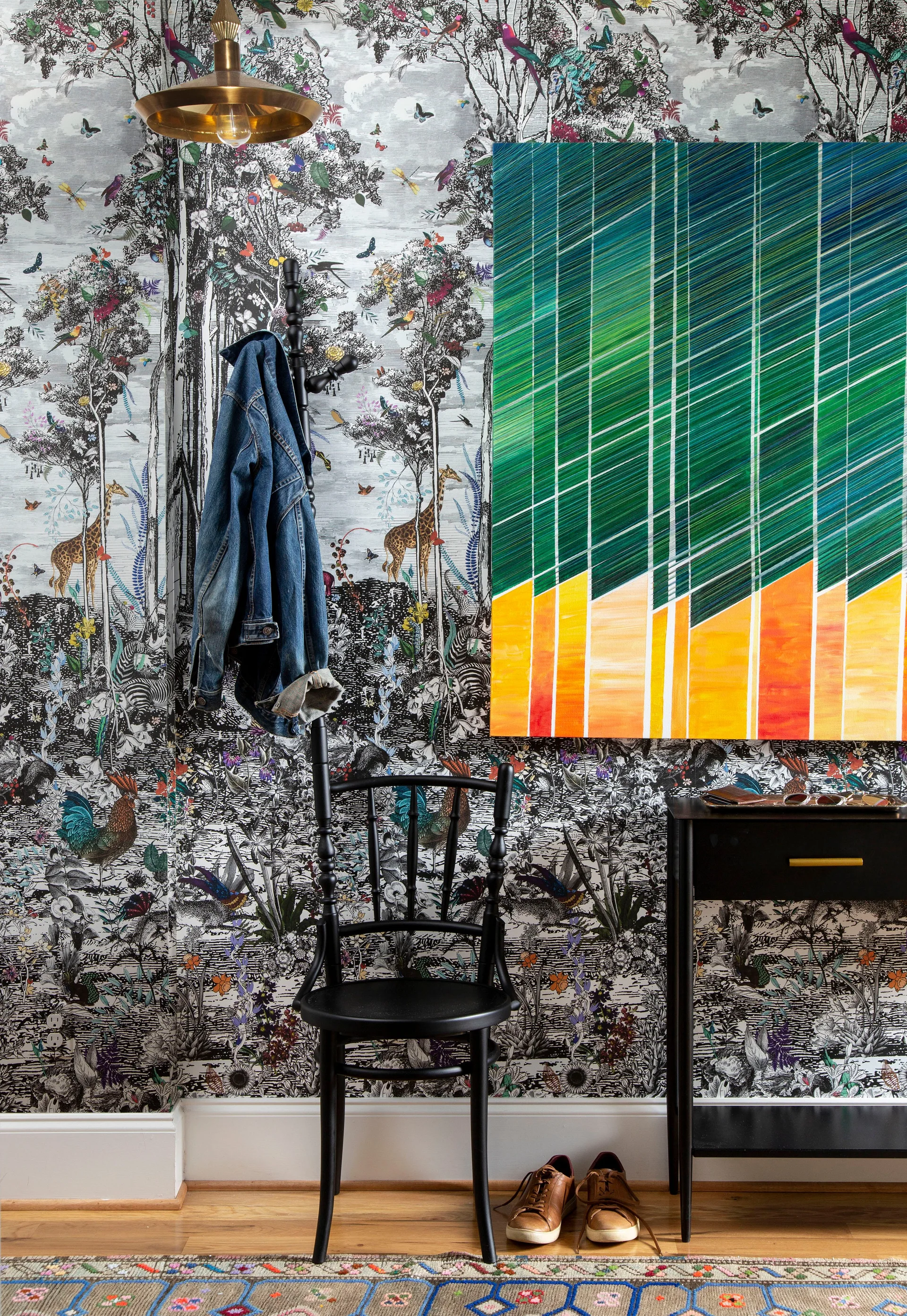 An entryway features black and white illustrated animal wallpaper, a black chair, a coat rack, and a large colorful abstract painting.