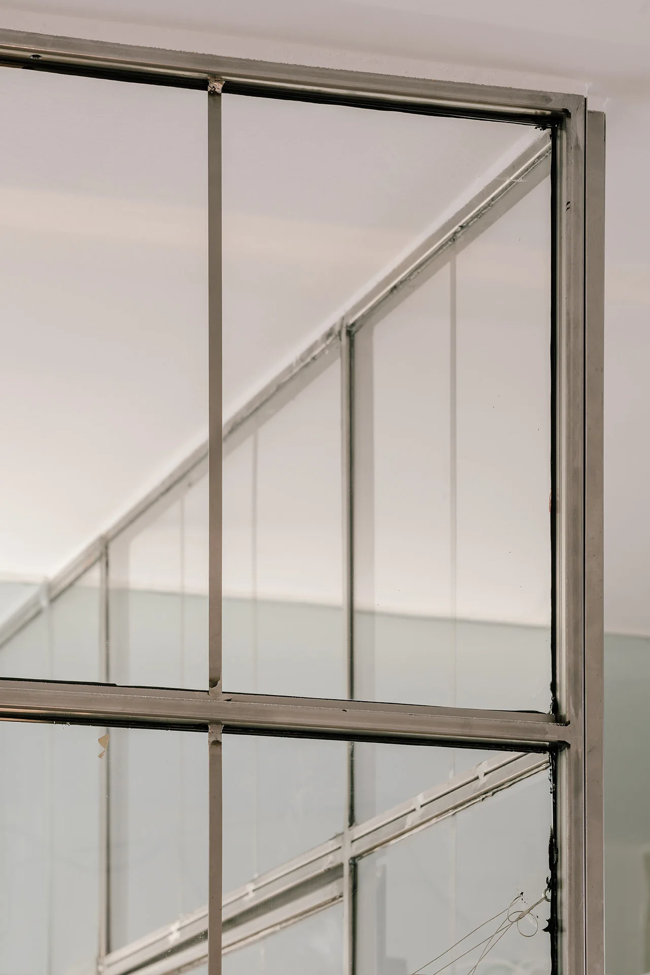 A close-up of a silver metal-framed glass partition wall with a grid pattern against a plain white ceiling and staircase.