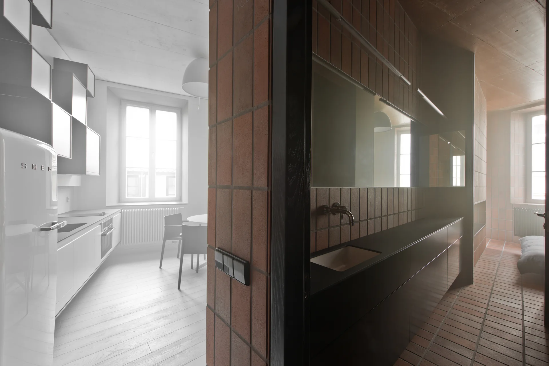 A split view showing a bright white kitchen on the left and a dark vanity with terracotta wall and floor tiles on the right.