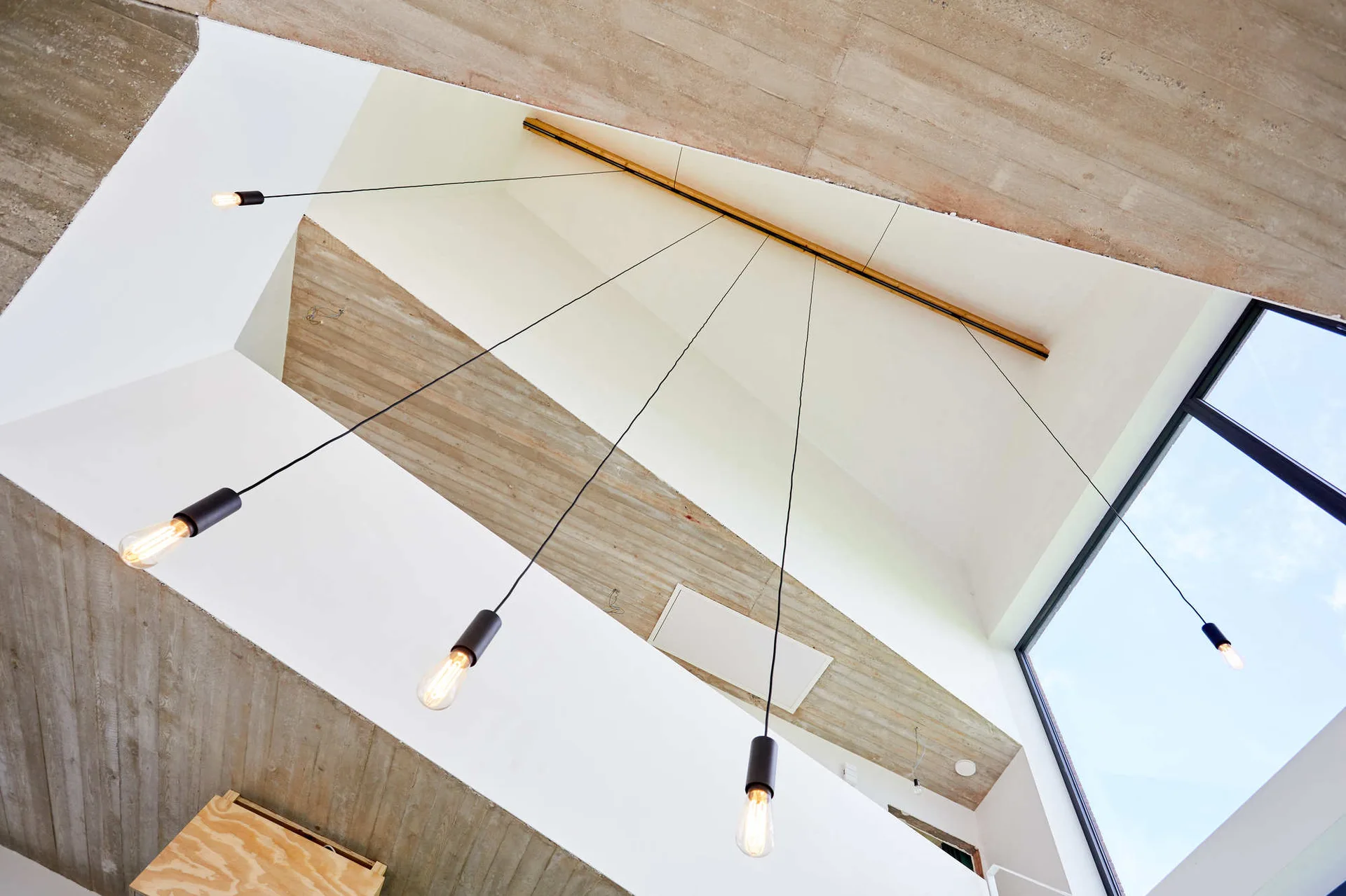 An upward view of a vaulted concrete ceiling with smooth white walls and minimalist black pendant lights hanging from long cords.