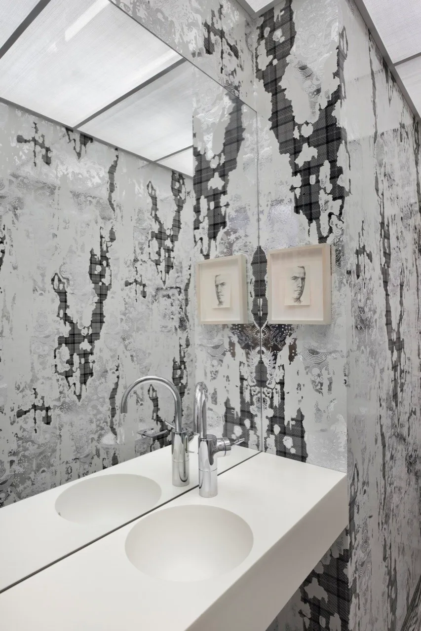 A modern bathroom features a floating white vanity with a chrome faucet against a high-contrast black and white patterned wall with a large mirror.