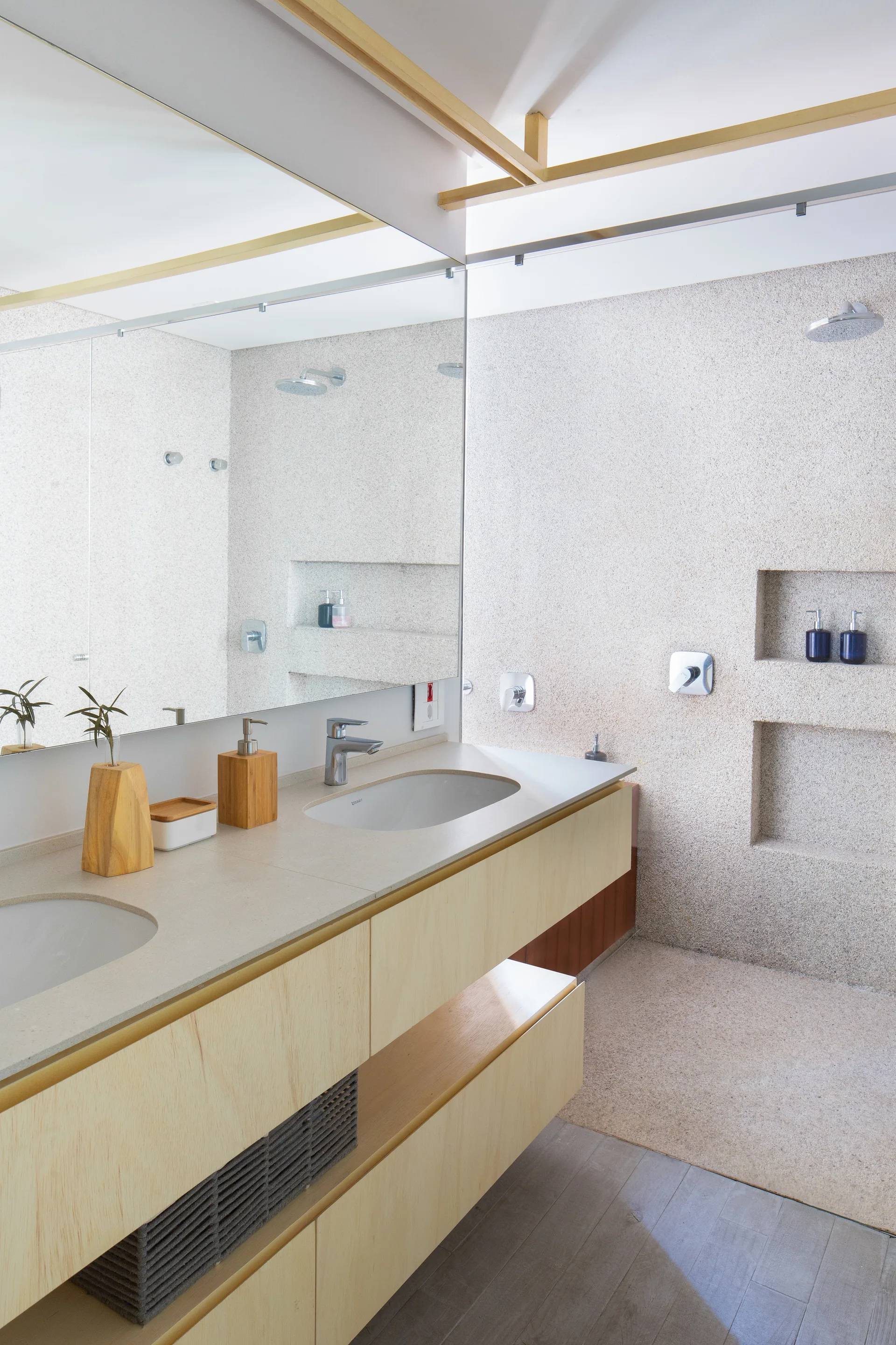 A bathroom with a floating light-wood double vanity, large mirror, and a walk-in shower featuring pebbled beige walls and recessed storage niches.