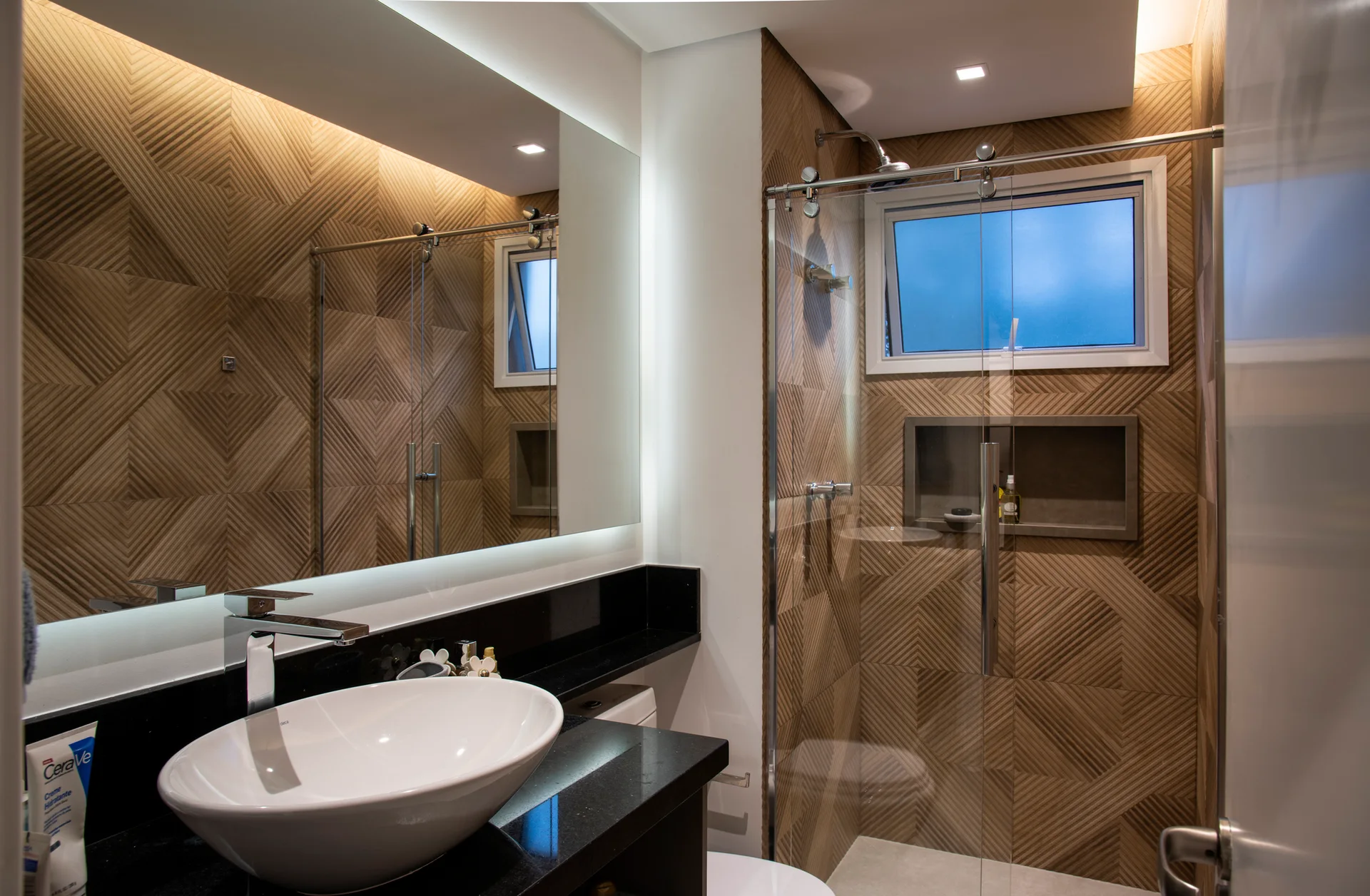 A modern bathroom featuring geometric wood-toned wall tiles, a black vanity with a white vessel sink, and a glass-enclosed shower.