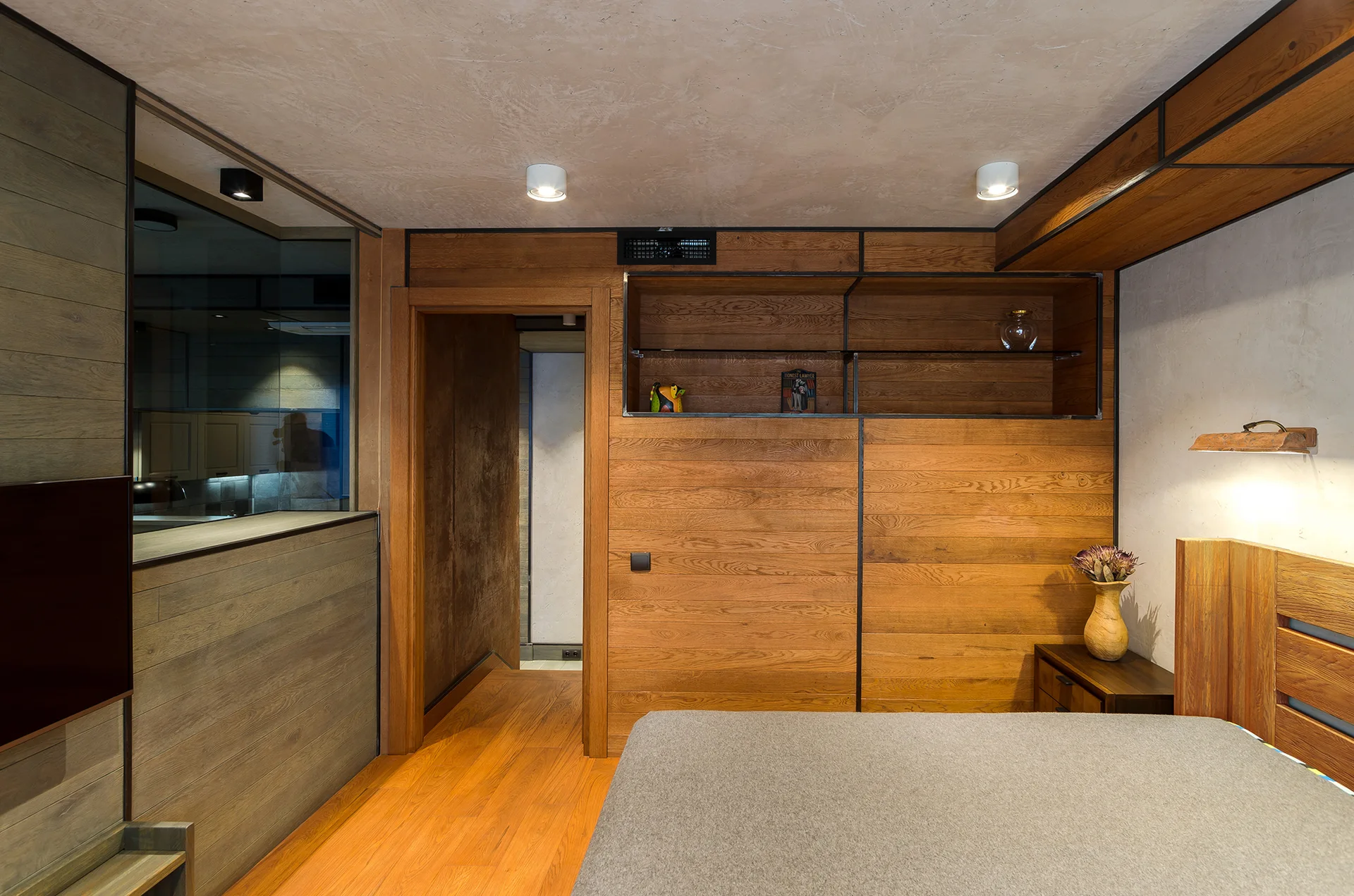 A modern bedroom with horizontal wood paneling, an integrated wall shelf, a grey bed, and a textured plaster ceiling.