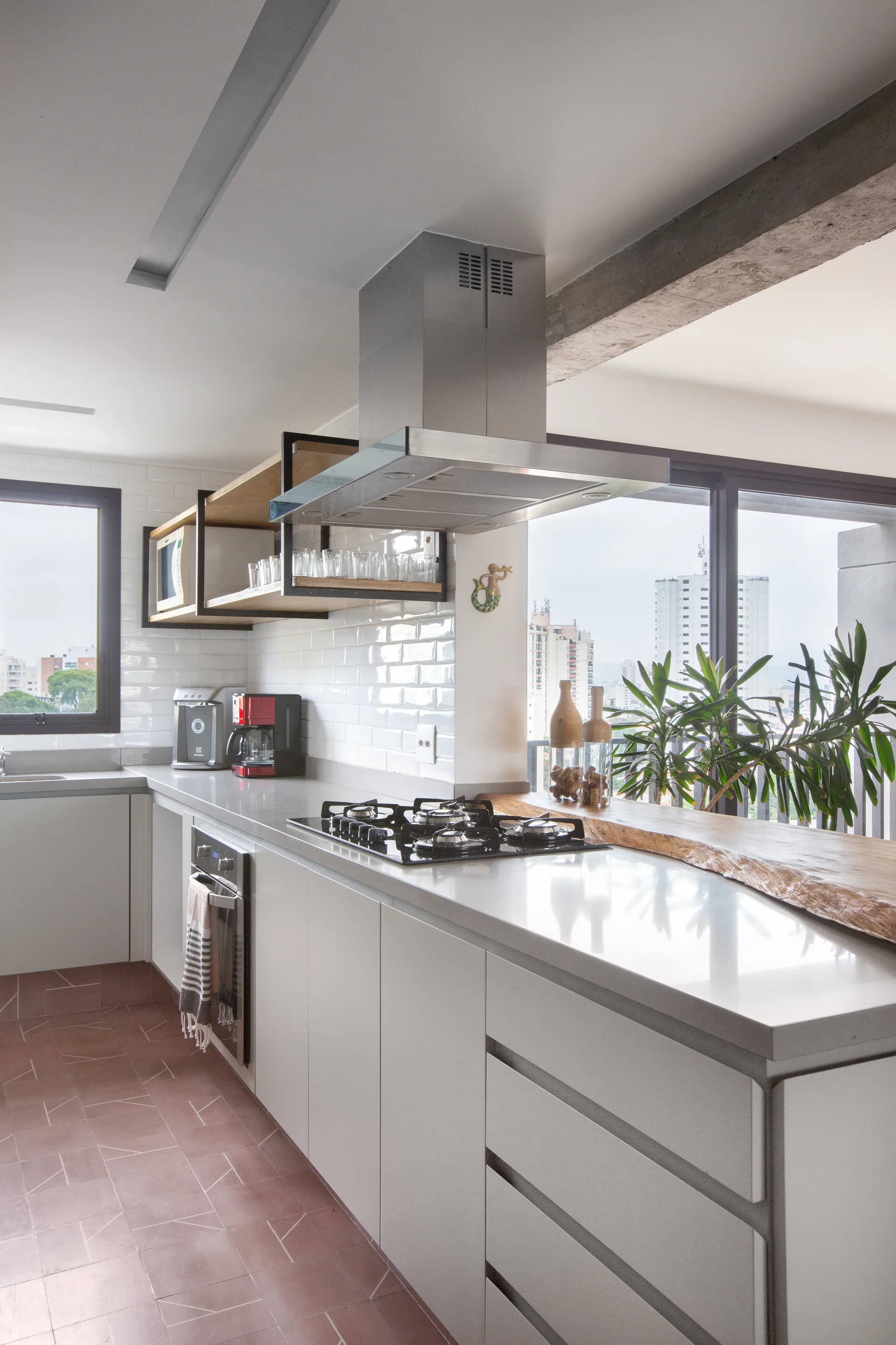 A modern kitchen features light gray lower cabinets, a live-edge wooden counter accent, white subway tile walls, and geometric terracotta floor tiles.