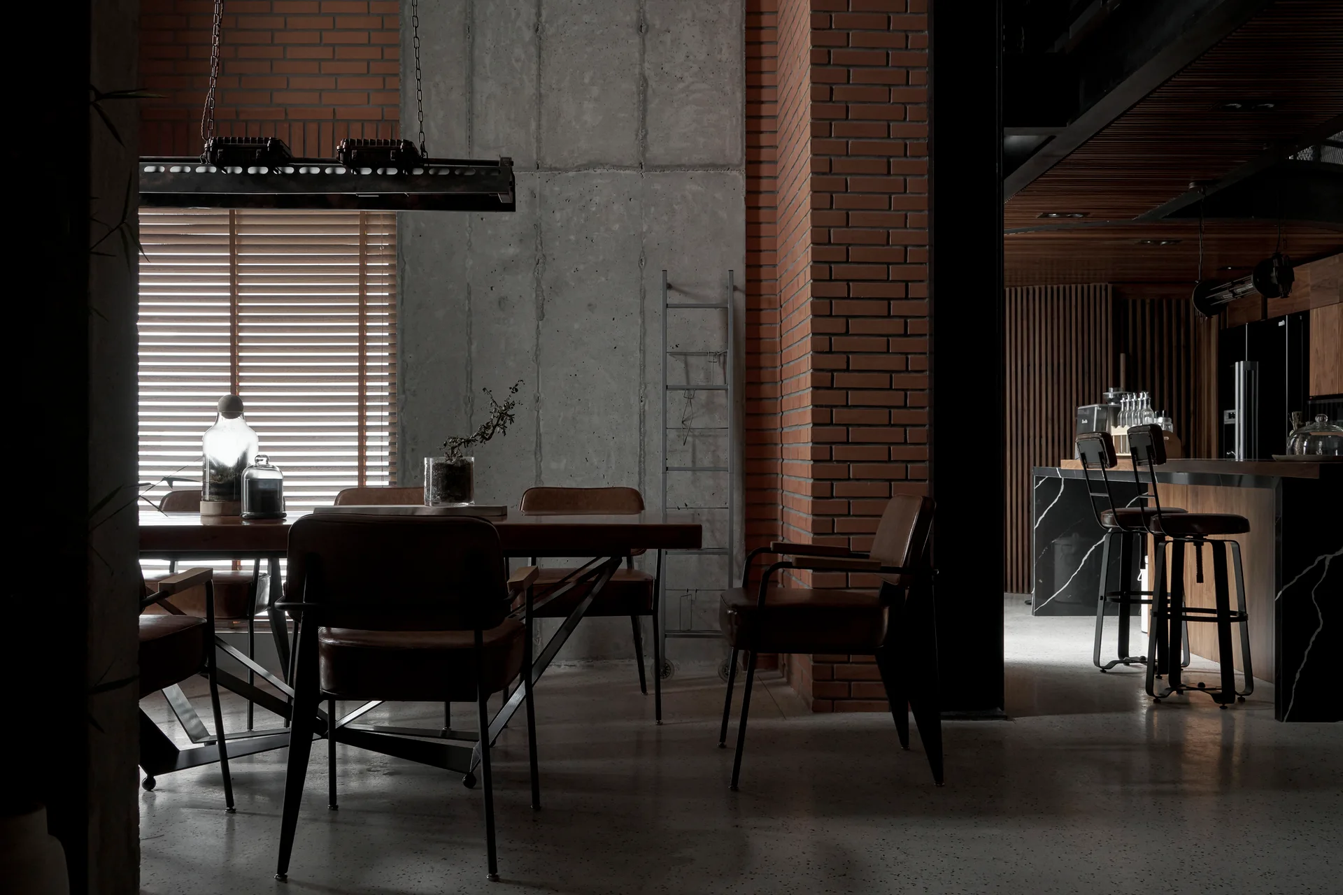 An industrial dining room features a wooden table with leather chairs set against walls of exposed red brick and smooth concrete.