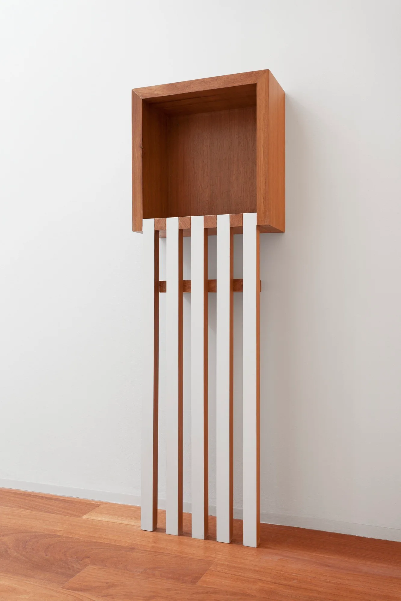 A modern wall-mounted wooden cubby shelf features white vertical slats extending to the light brown wood floor against a white wall.