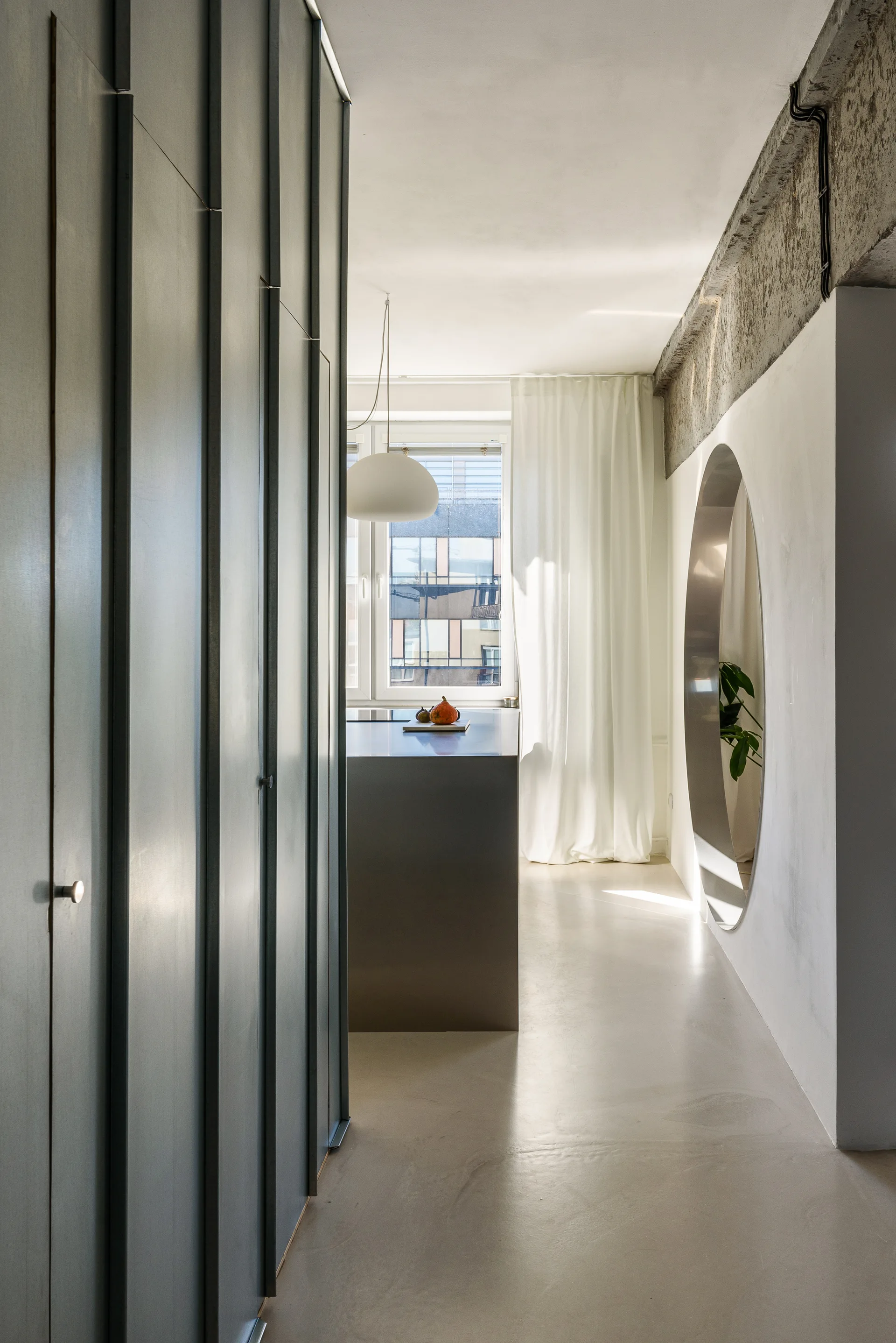 A minimalist kitchen features dark grey integrated cabinetry, a central island, and a white wall with a large circular cutout.