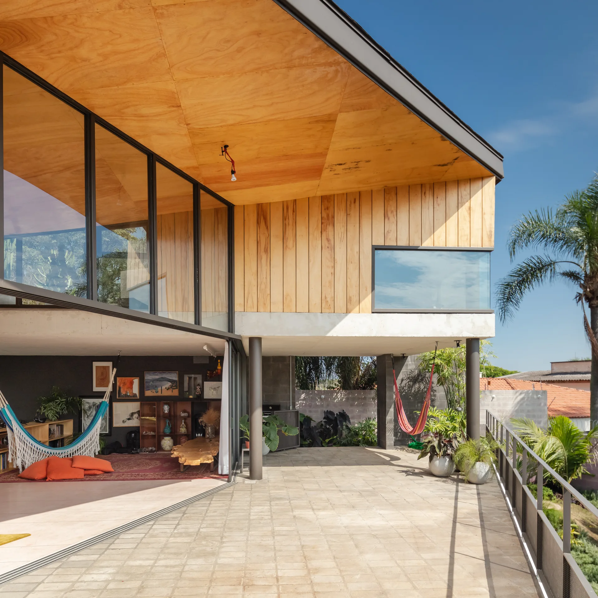 A modern patio features paved tiling, a warm wood-paneled ceiling, sliding glass doors opening to an indoor room, and a hanging hammock.