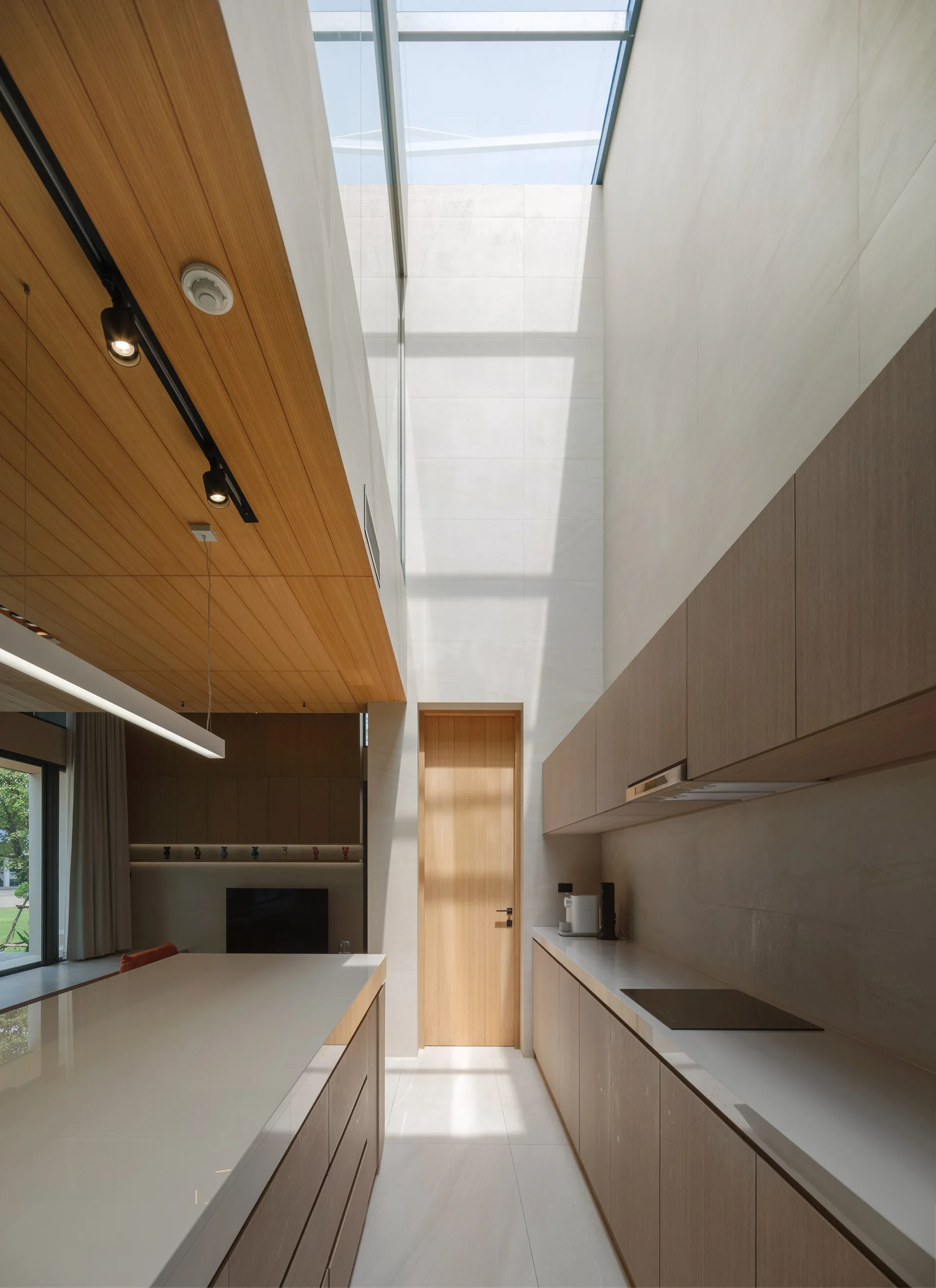 A minimalist kitchen with light wood cabinetry and a white countertop island beneath a soaring skylight and wood paneled ceiling.