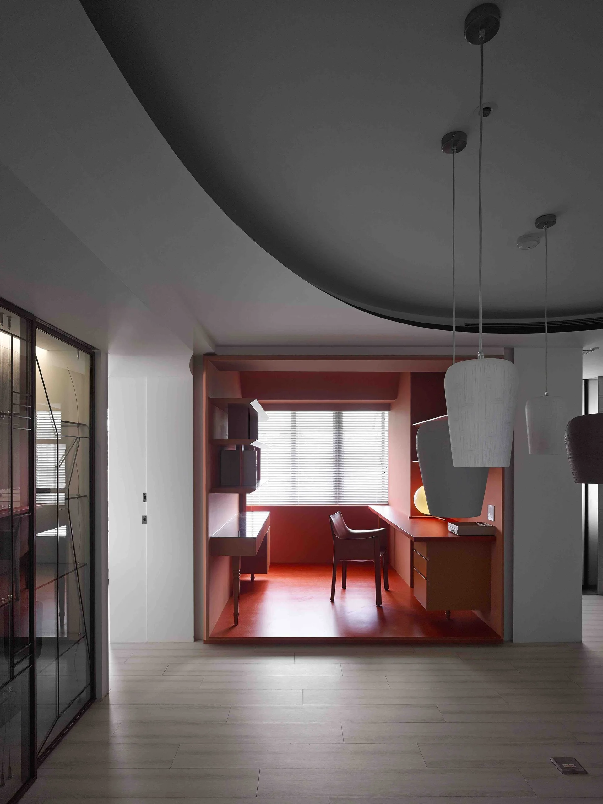 A recessed home office alcove painted entirely in terracotta red features a built-in desk, a leather chair, and window blinds.