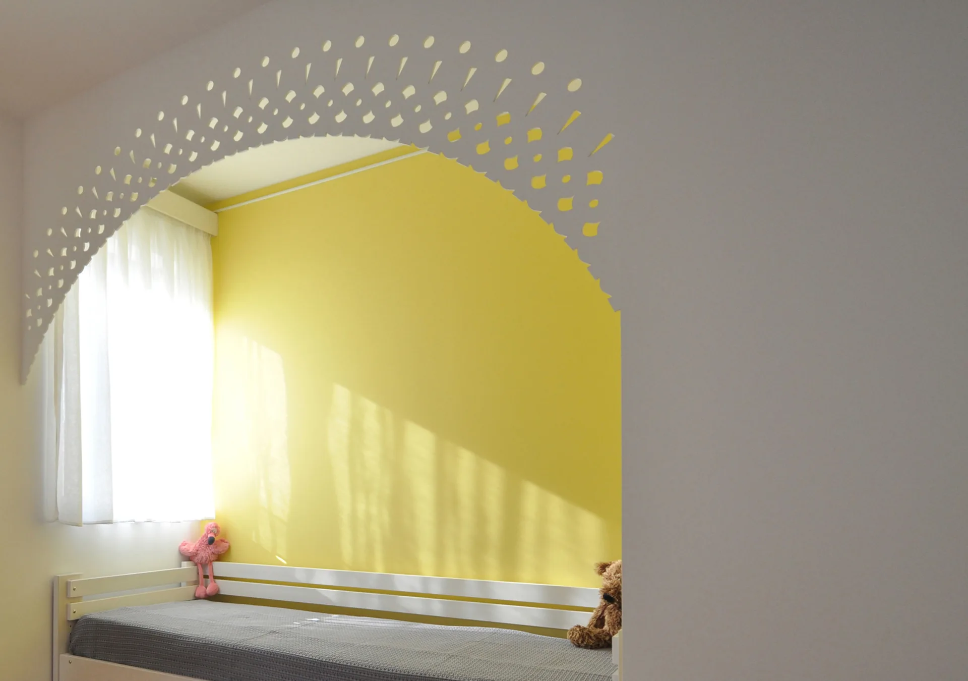 A white daybed is nestled inside a bright yellow alcove framed by a decorative white arched partition with small patterned cutouts.
