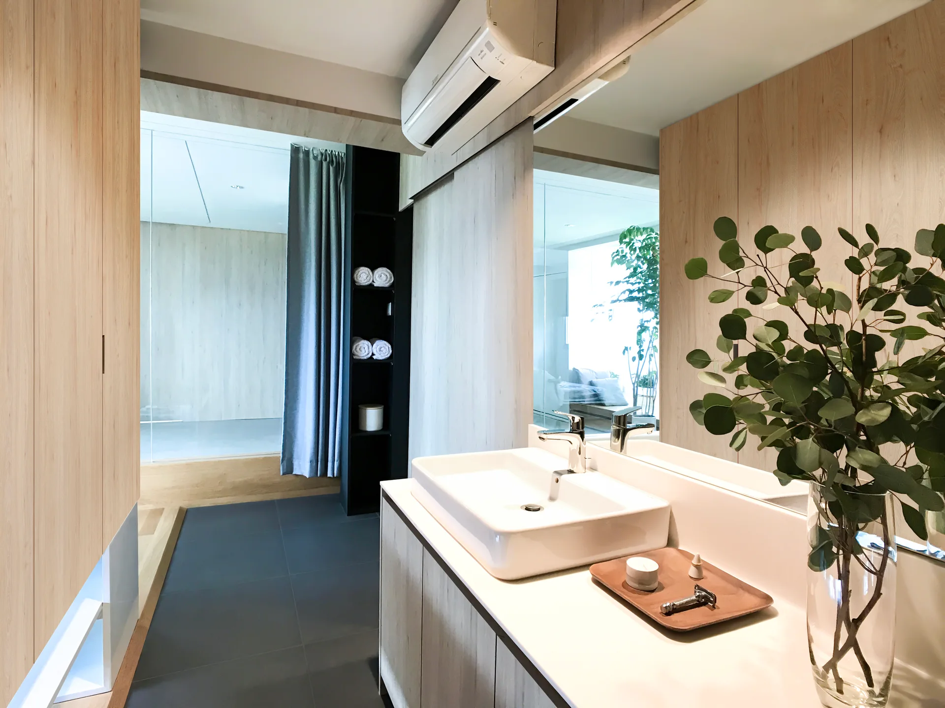 A minimalist bathroom with a light wood vanity, a rectangular white vessel sink, a large mirror, and dark grey tile flooring.